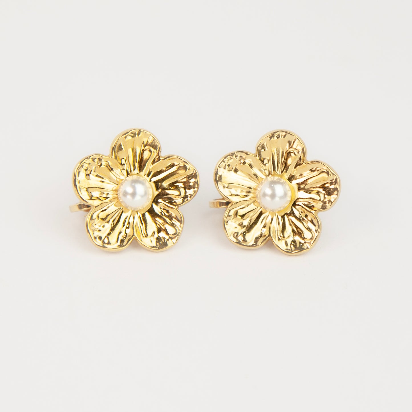 Pair of gold-toned non-pierced flower clip-on stud earrings with textured petals, white faux pearl center, and paddle back clip mechanism.