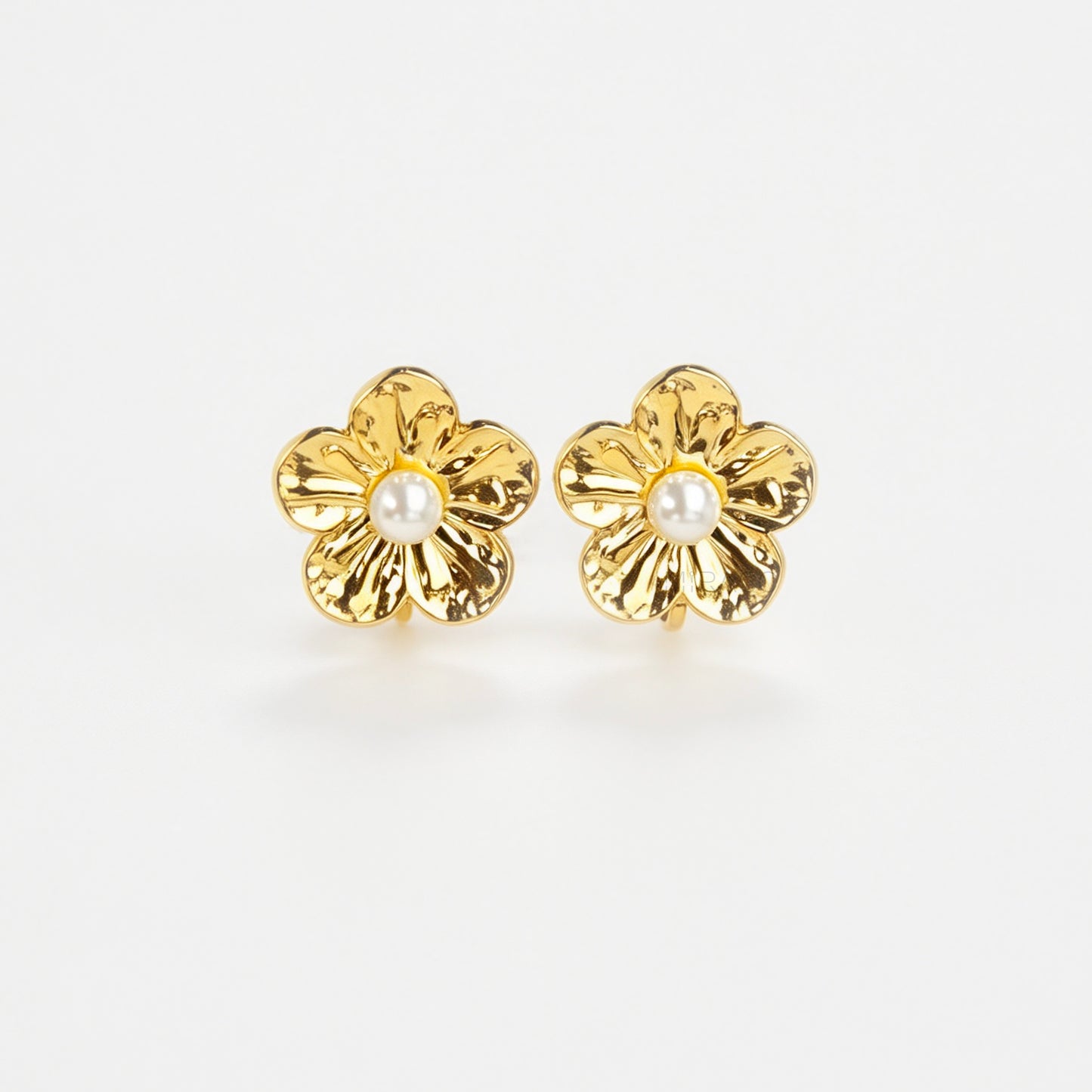 Pair of gold-toned non-pierced flower clip-on stud earrings with textured petals, white faux pearl center, and paddle back clip mechanism.