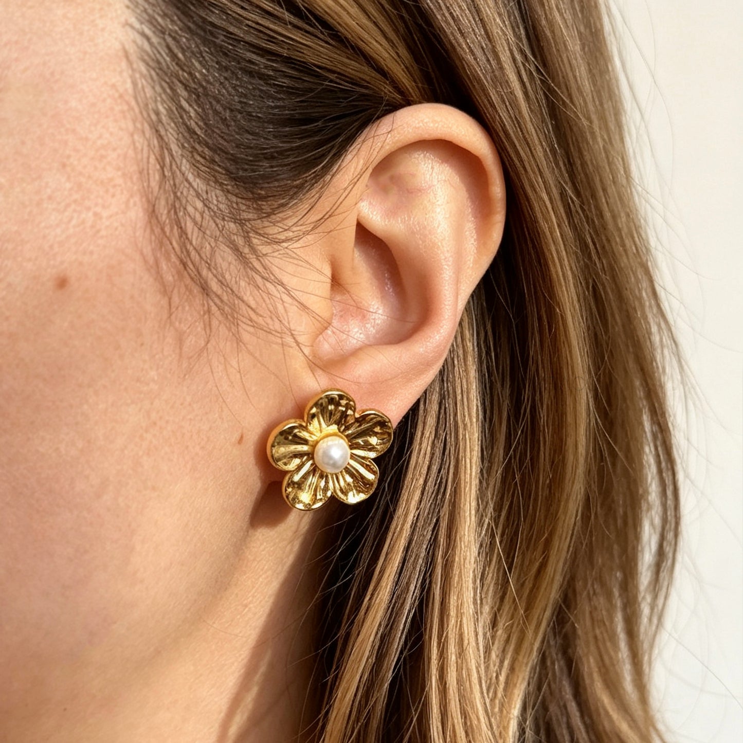 Pair of gold-toned non-pierced flower clip-on stud earrings with textured petals, white faux pearl center, and paddle back clip mechanism.