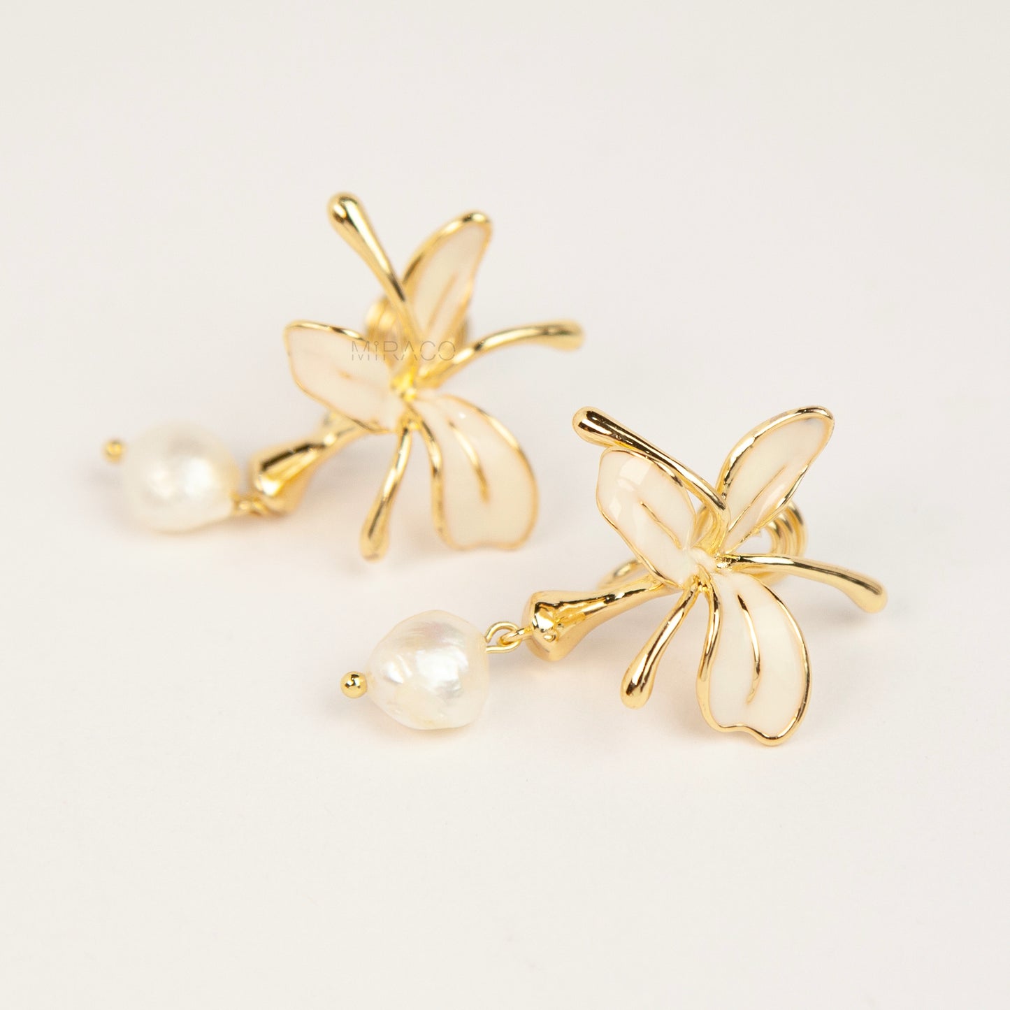 Pair of gold-toned non-pierced clip-on earrings featuring cream enamel floral petals with dangling genuine freshwater pearls and spiral coil backs.