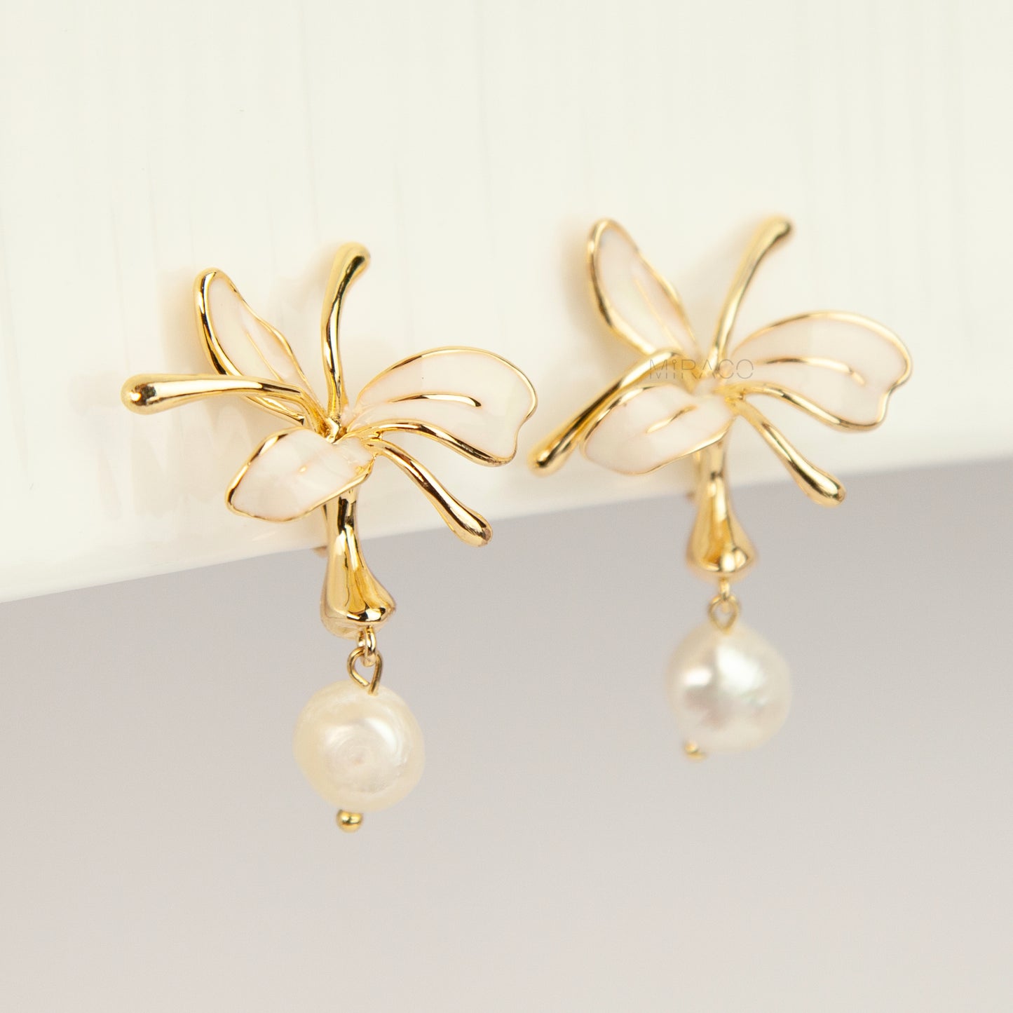 Pair of gold-toned non-pierced clip-on earrings featuring cream enamel floral petals with dangling genuine freshwater pearls and spiral coil backs.