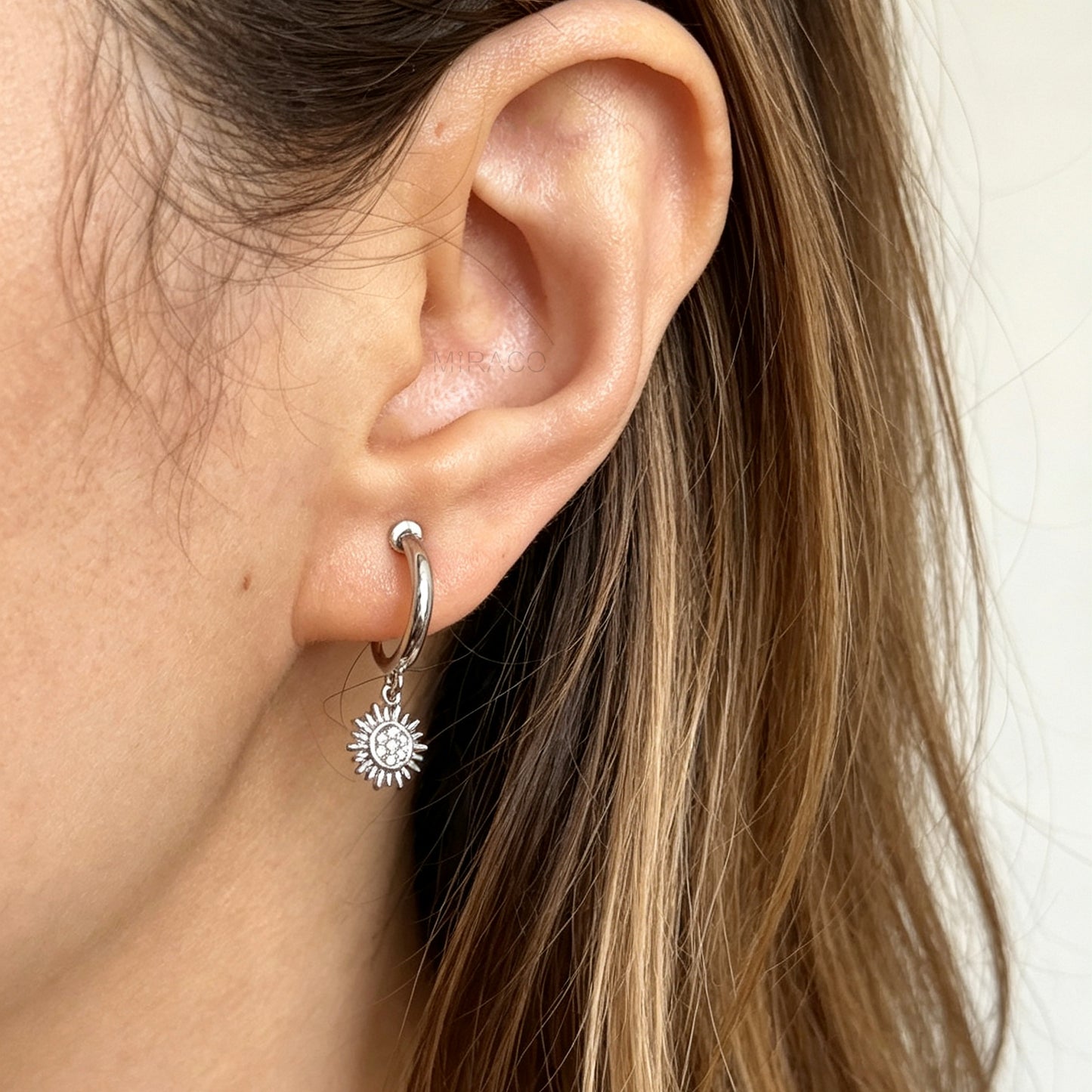 silver-toned non-pierced clip-on hoop earrings featuring dangling pave crystal sunburst charms and silicone-padded spiral coil backs.