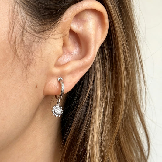 silver-toned non-pierced clip-on hoop earrings featuring dangling pave crystal sunburst charms and silicone-padded spiral coil backs.