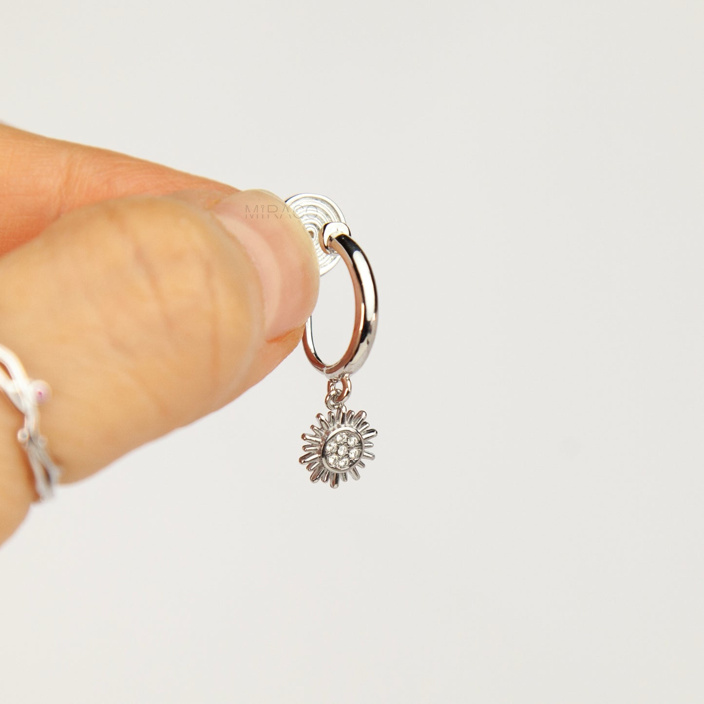 silver-toned non-pierced clip-on hoop earrings featuring dangling pave crystal sunburst charms and silicone-padded spiral coil backs.