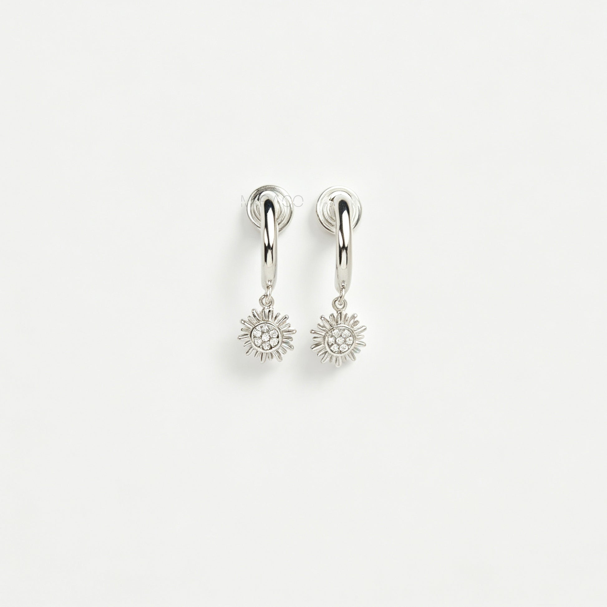 Pair of silver-toned non-pierced clip-on hoop earrings featuring dangling pave crystal sunburst charms and silicone-padded spiral coil backs.