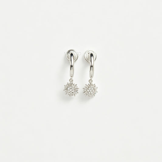Pair of silver-toned non-pierced clip-on hoop earrings featuring dangling pave crystal sunburst charms and silicone-padded spiral coil backs.