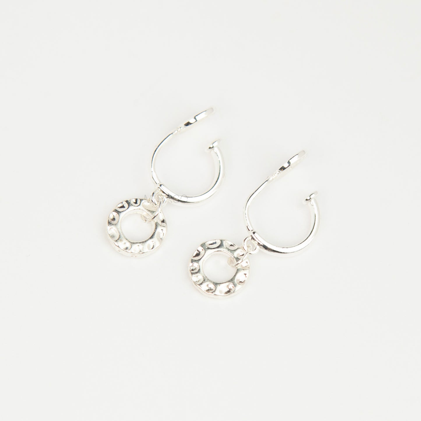 Pair of silver-toned non-pierced clip-on hoop earrings with dangling textured open circle discs and clear silicone spiral coil backs.