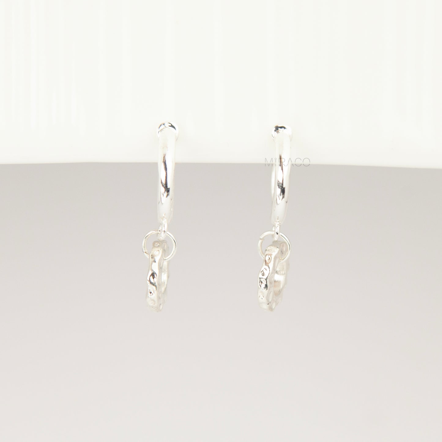 Pair of silver-toned non-pierced clip-on hoop earrings with dangling textured open circle discs and clear silicone spiral coil backs.
