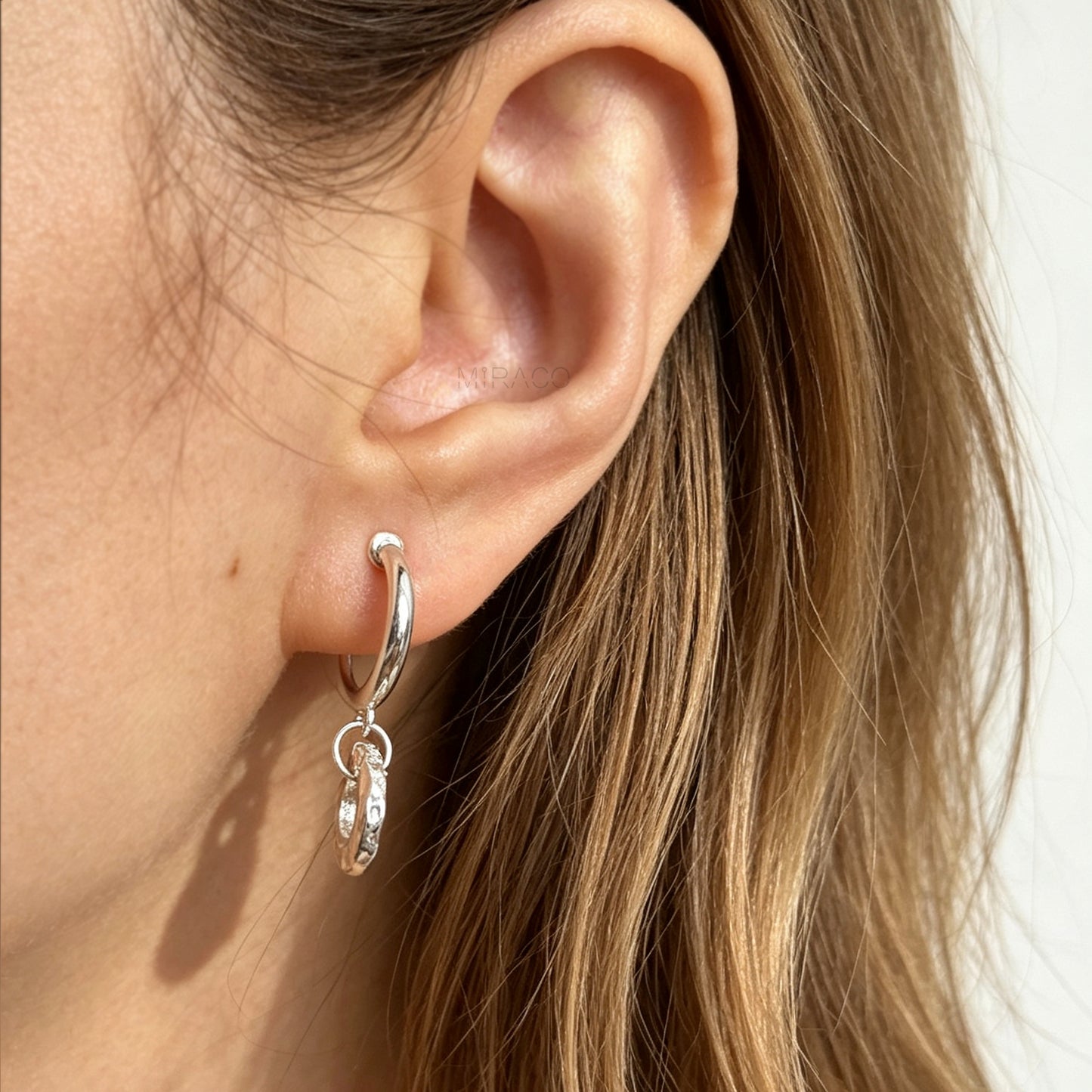 Pair of silver-toned non-pierced clip-on hoop earrings with dangling textured open circle discs and clear silicone spiral coil backs.