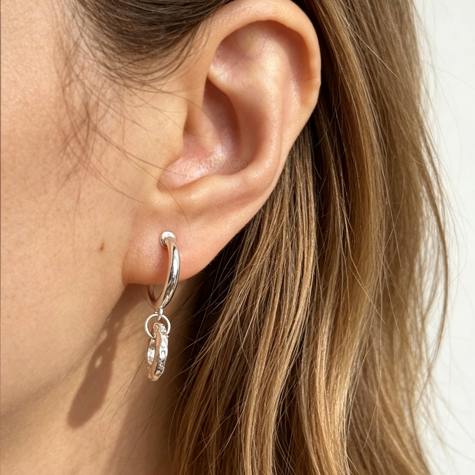 Pair of silver-toned non-pierced clip-on hoop earrings with dangling textured open circle discs and clear silicone spiral coil backs.