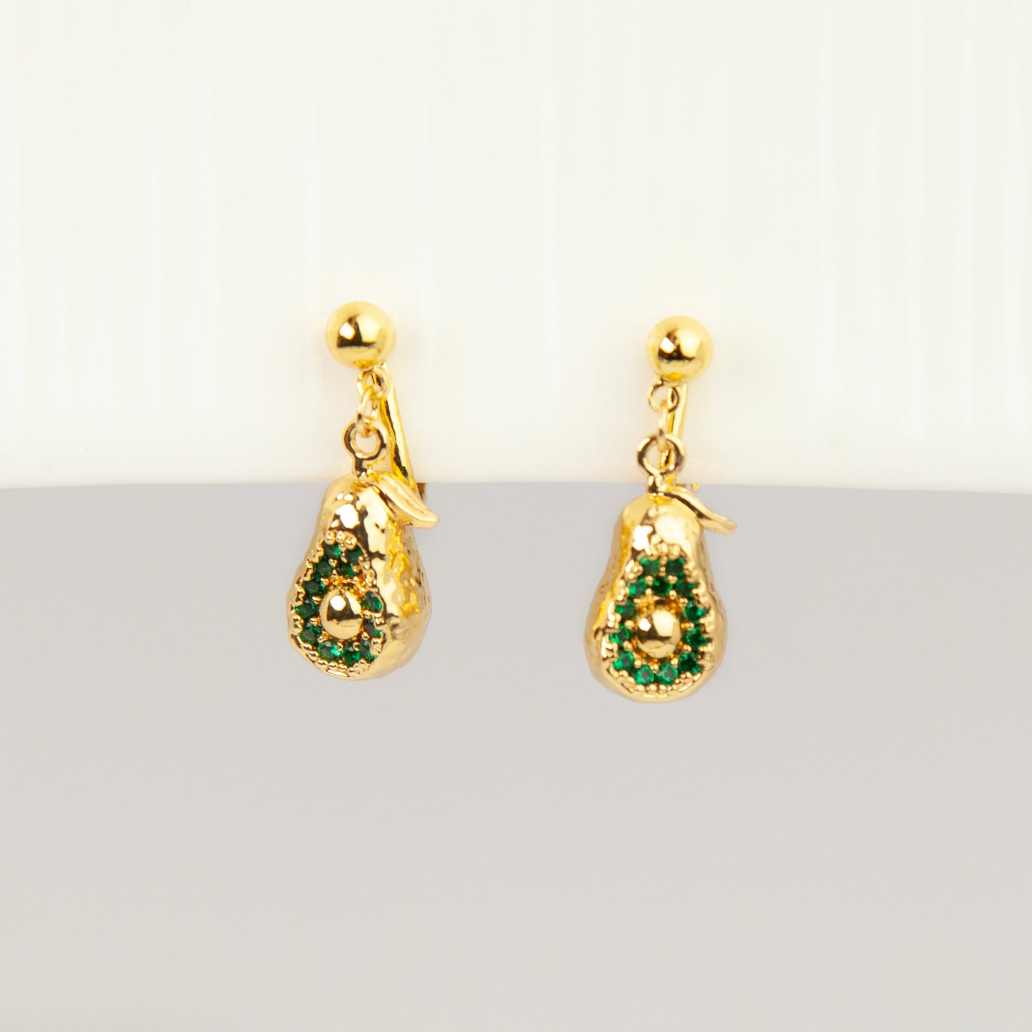 Pair of gold-toned non-pierced avocado clip-on drop earrings with green crystal accents and adjustable screw-back mechanisms.