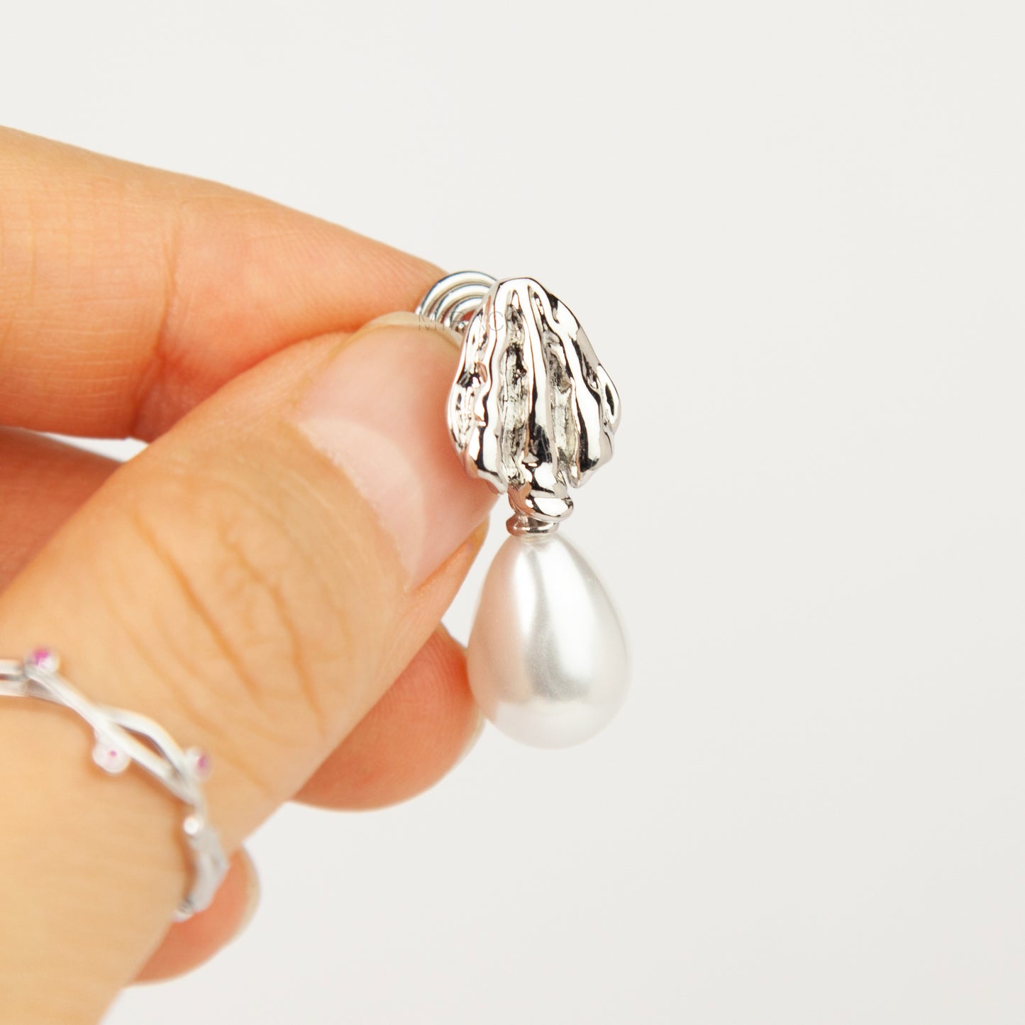 Pair of gold and silver textured shell clip-on earrings featuring white teardrop faux pearls with pain-free coil backs for non-pierced ears displayed against a clean white background.