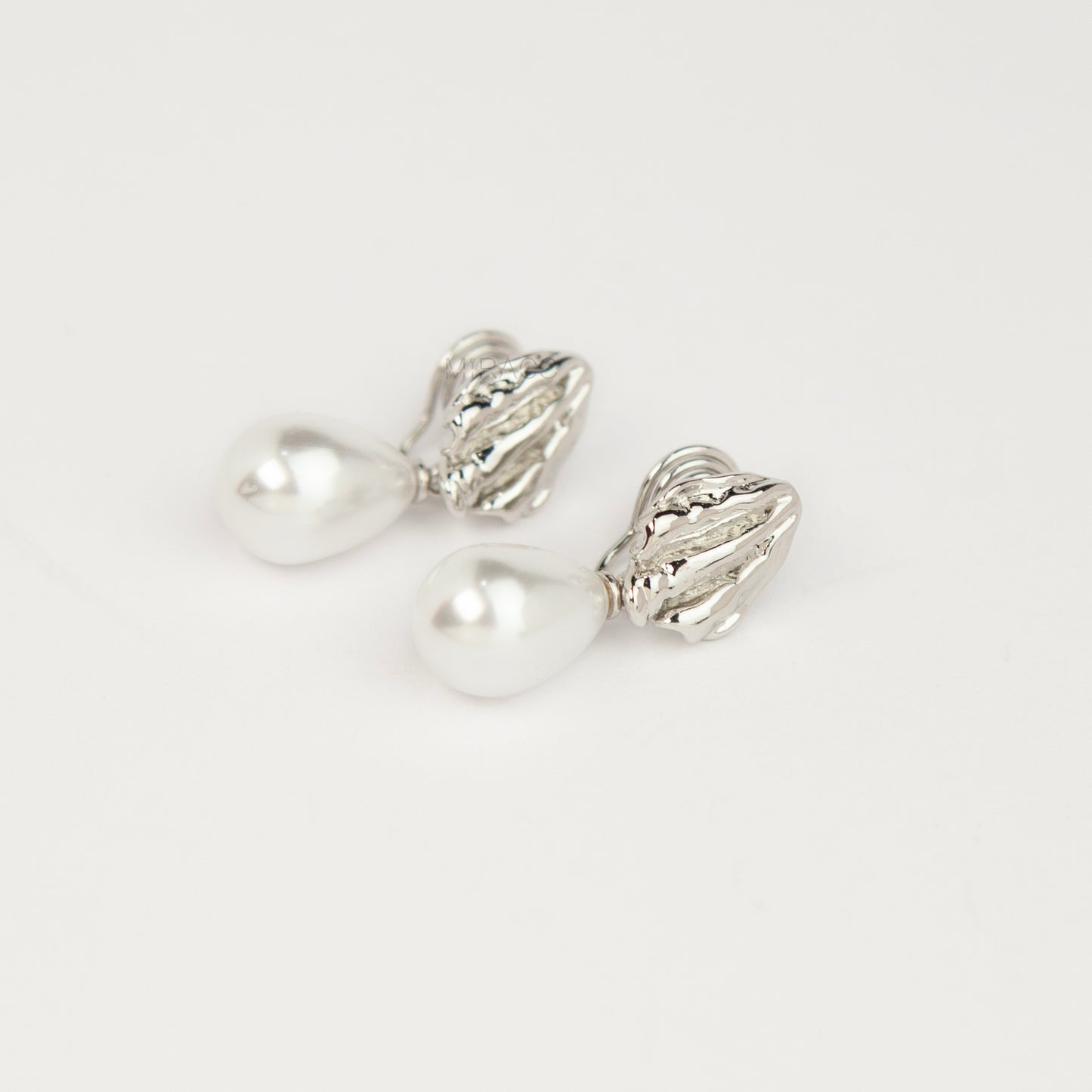 Pair of gold and silver textured shell clip-on earrings featuring white teardrop faux pearls with pain-free coil backs for non-pierced ears displayed against a clean white background.