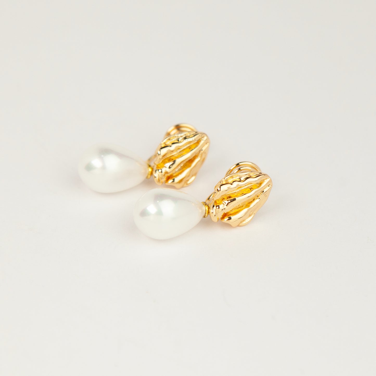 Pair of gold and silver textured shell clip-on earrings featuring white teardrop faux pearls with pain-free coil backs for non-pierced ears displayed against a clean white background.