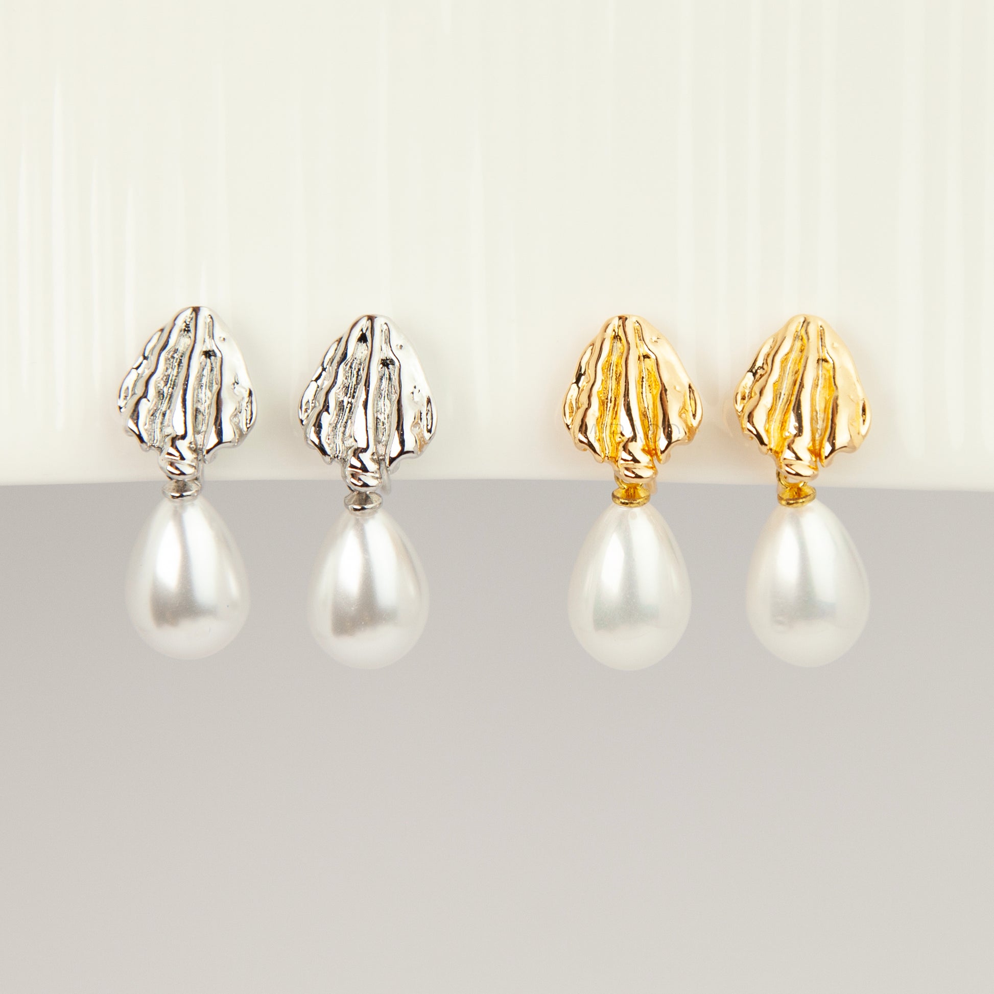 Pair of gold and silver textured shell clip-on earrings featuring white teardrop faux pearls with pain-free coil backs for non-pierced ears displayed against a clean white background.
