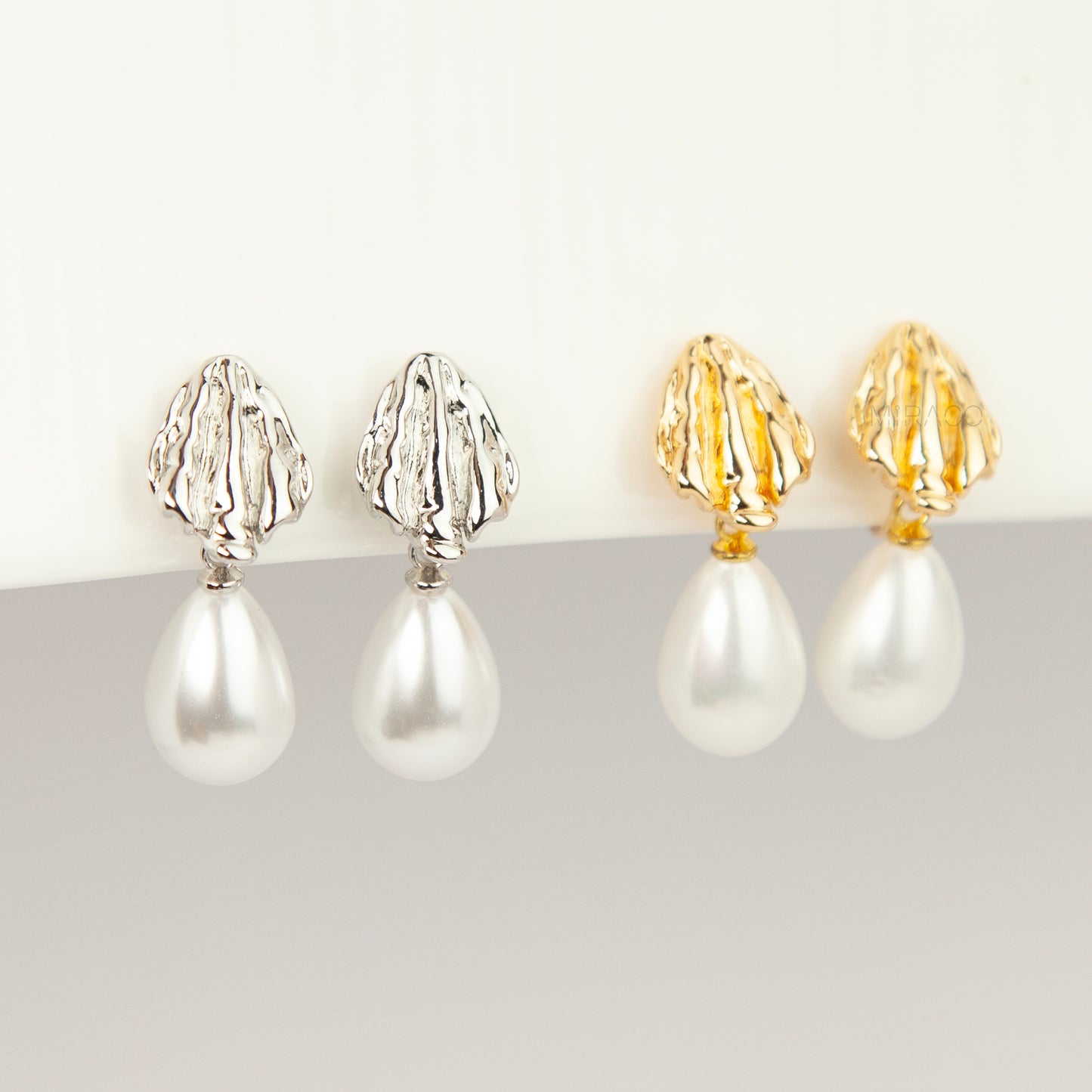 Pair of gold and silver textured shell clip-on earrings featuring white teardrop faux pearls with pain-free coil backs for non-pierced ears displayed against a clean white background.