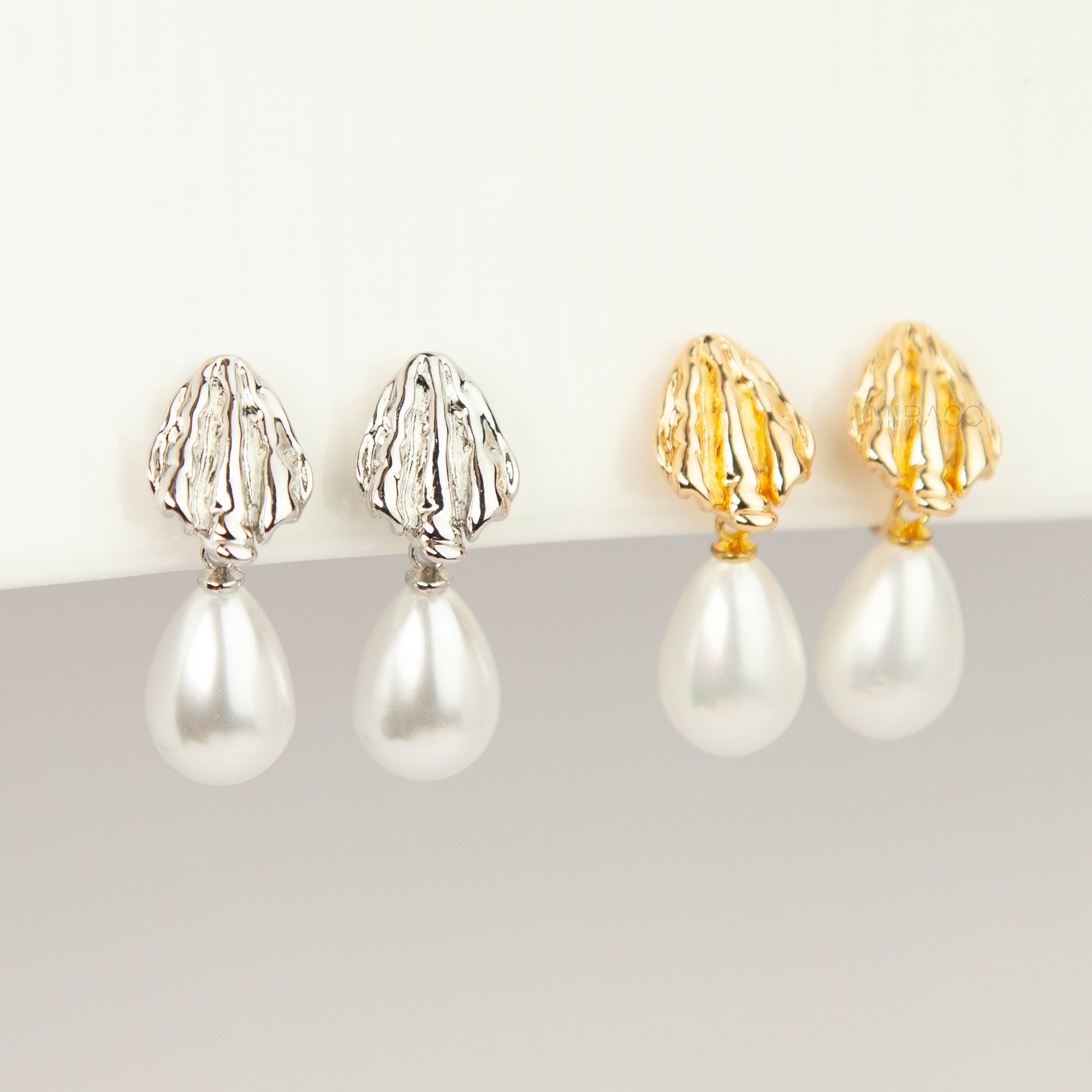 Pair of gold and silver textured shell clip-on earrings featuring white teardrop faux pearls with pain-free coil backs for non-pierced ears displayed against a clean white background.