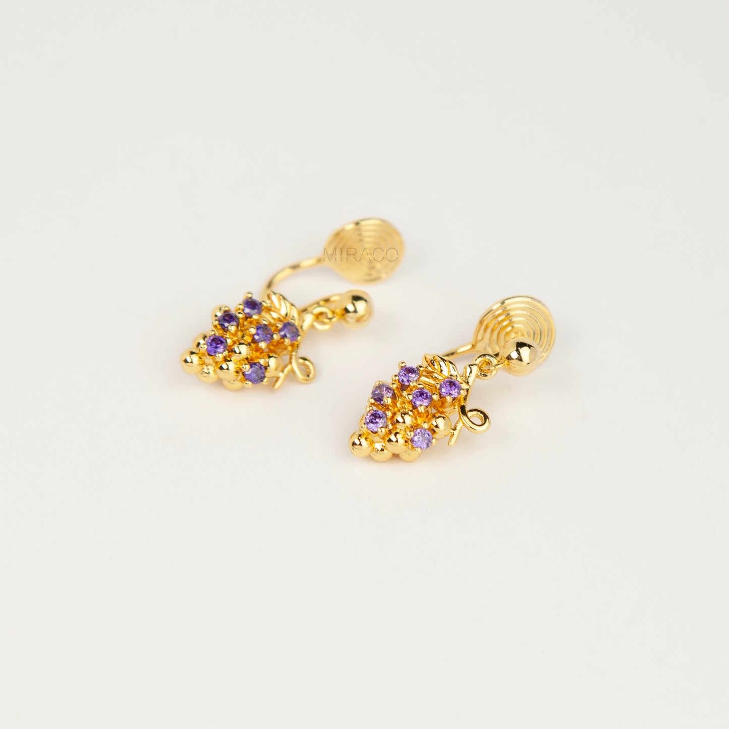 Pair of gold grape cluster clip-on drop earrings encrusted with purple crystals featuring pain-free coil backs for non-pierced ears on a white background.