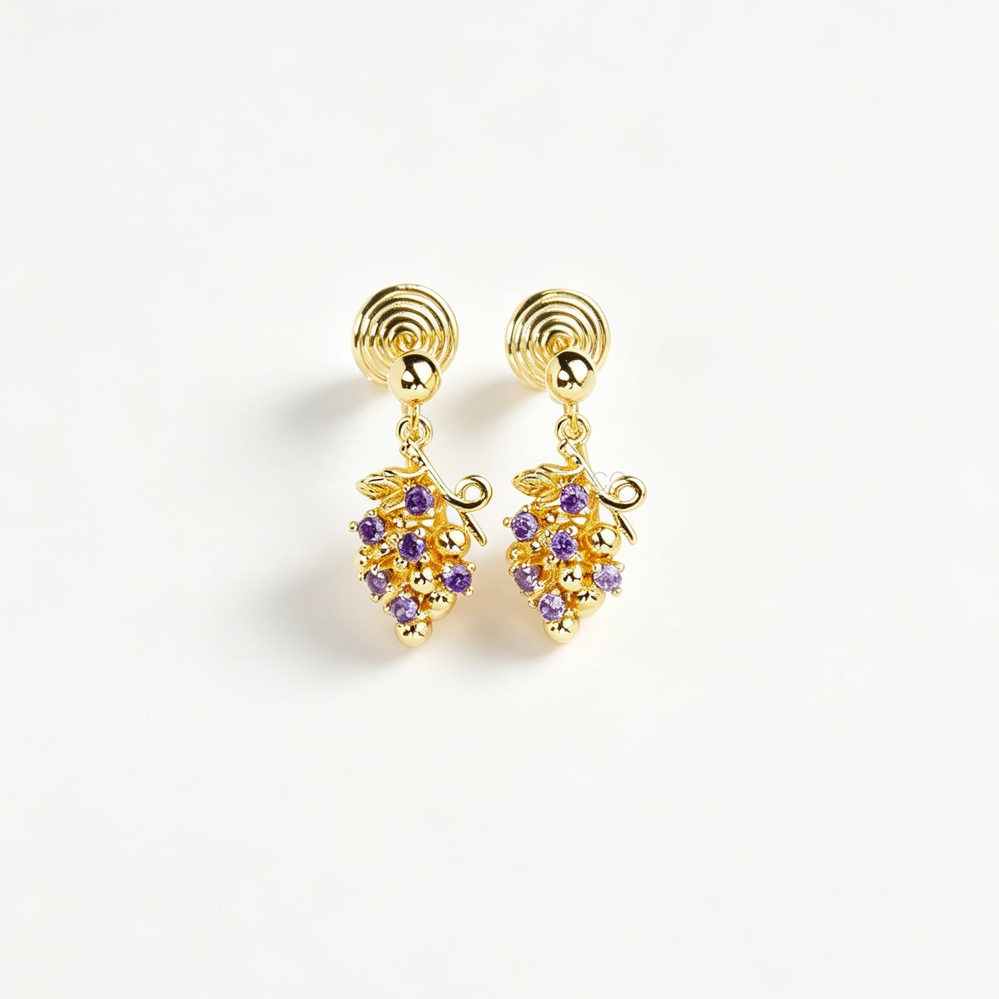 Pair of gold grape cluster clip-on drop earrings encrusted with purple crystals featuring pain-free coil backs for non-pierced ears on a white background.
