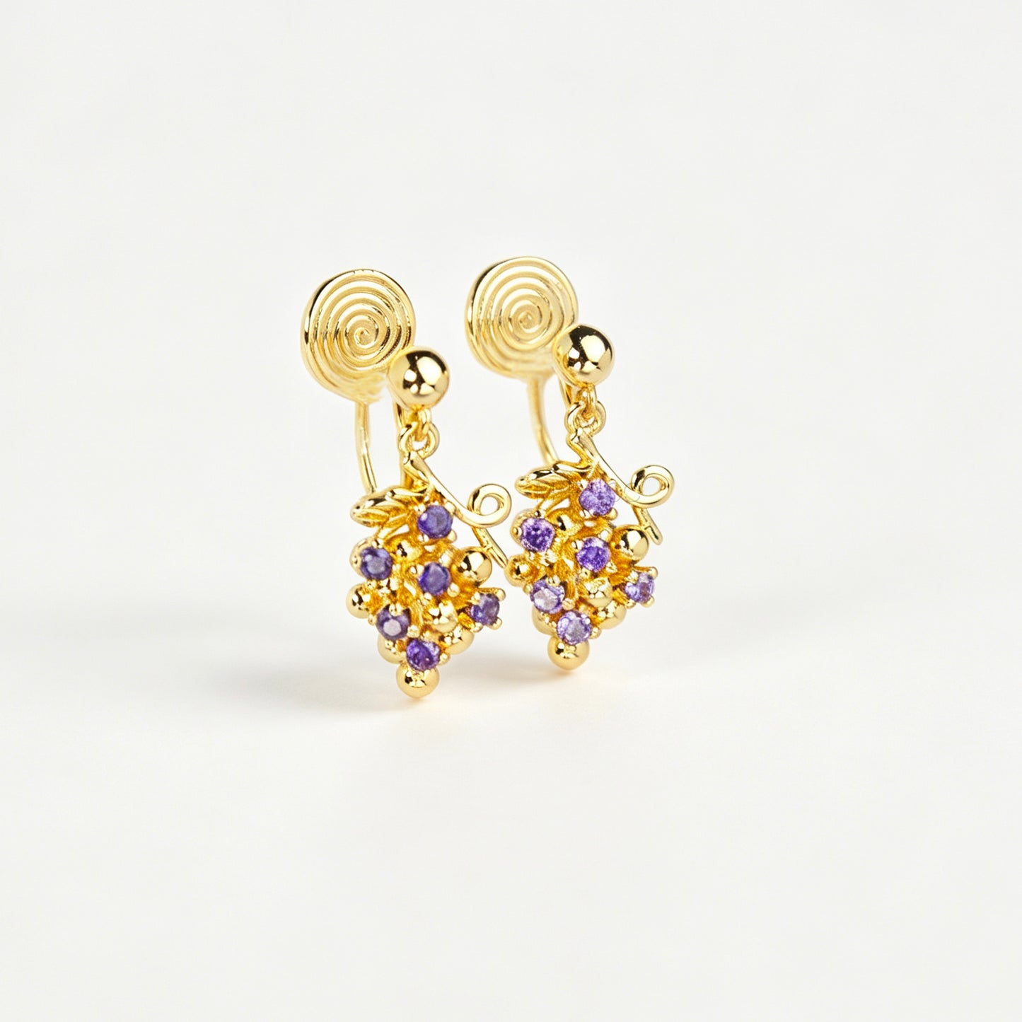 Pair of gold grape cluster clip-on drop earrings encrusted with purple crystals featuring pain-free coil backs for non-pierced ears on a white background.