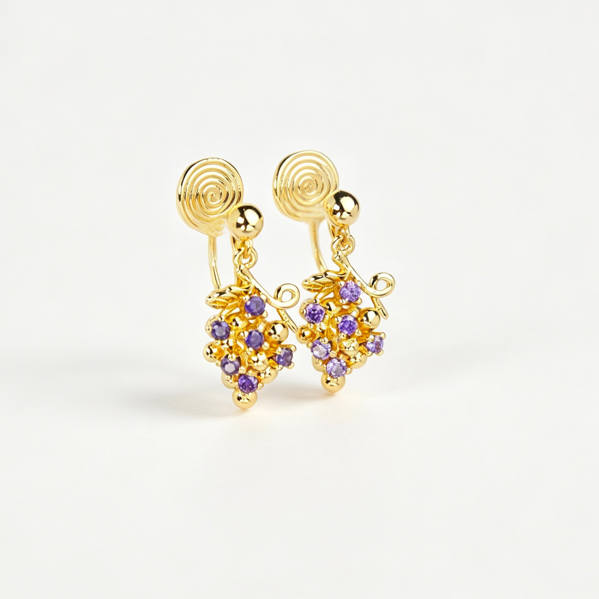 Pair of gold grape cluster clip-on drop earrings encrusted with purple crystals featuring pain-free coil backs for non-pierced ears on a white background.
