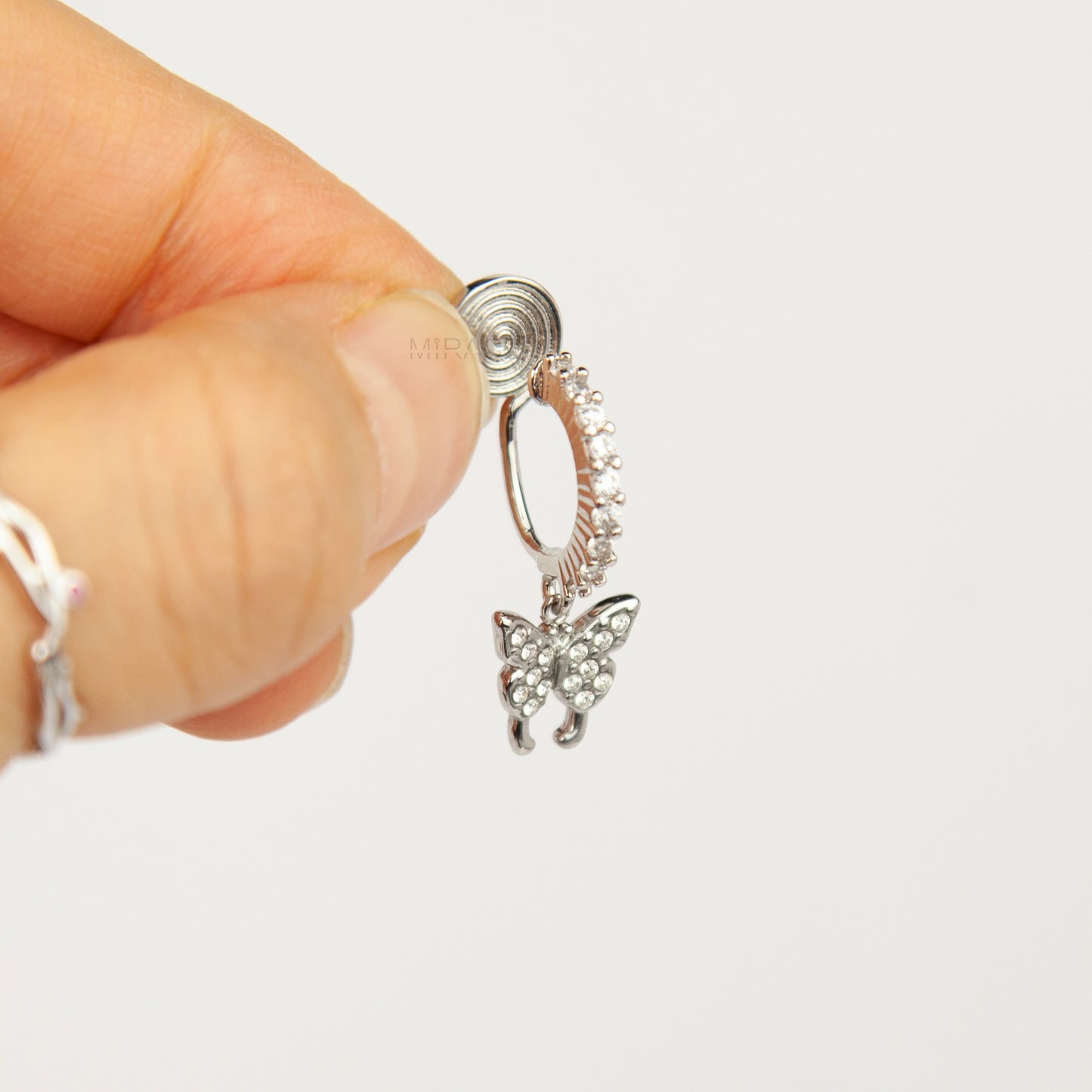 Pair of silver clip-on huggie hoop earrings featuring pavé cubic zirconia butterfly charms and pain-free coil backs for non-pierced ears against a white background.