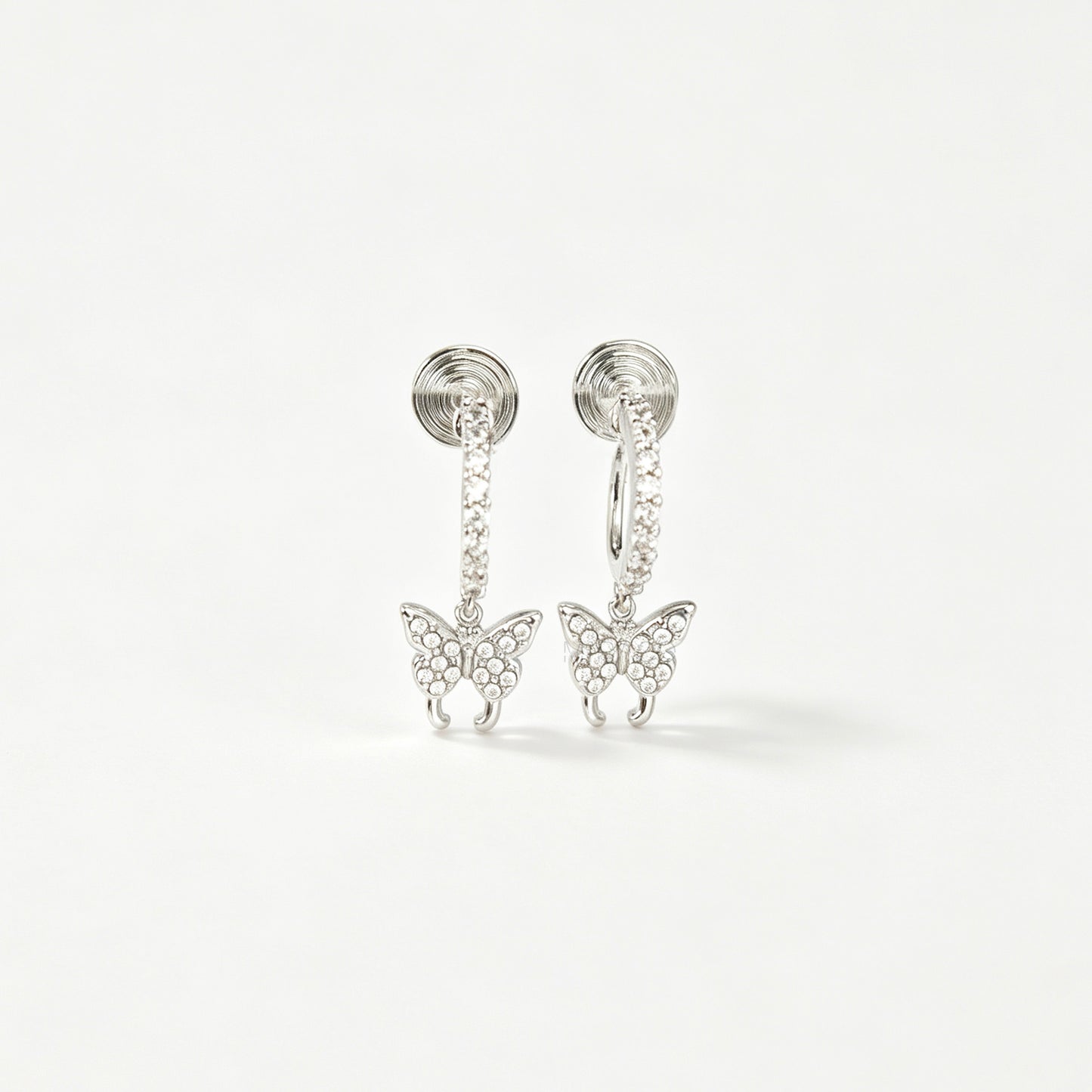 Pair of silver clip-on huggie hoop earrings featuring pavé cubic zirconia butterfly charms and pain-free coil backs for non-pierced ears against a white background.