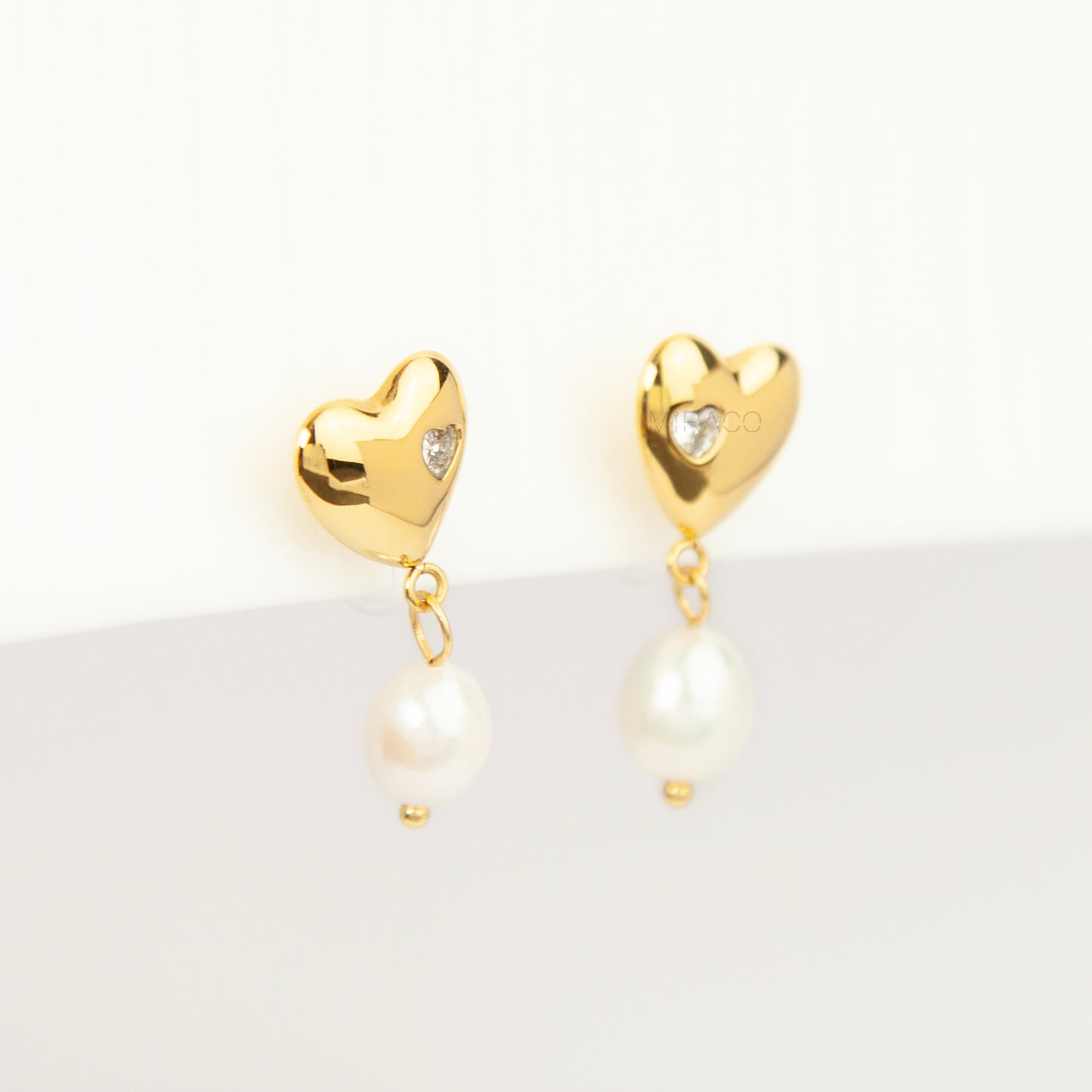 Pair of polished gold puffy heart clip-on earrings with star-set cz detail and dangling white pearls featuring clear invisible resin backs for non-pierced ears against a white backdrop.