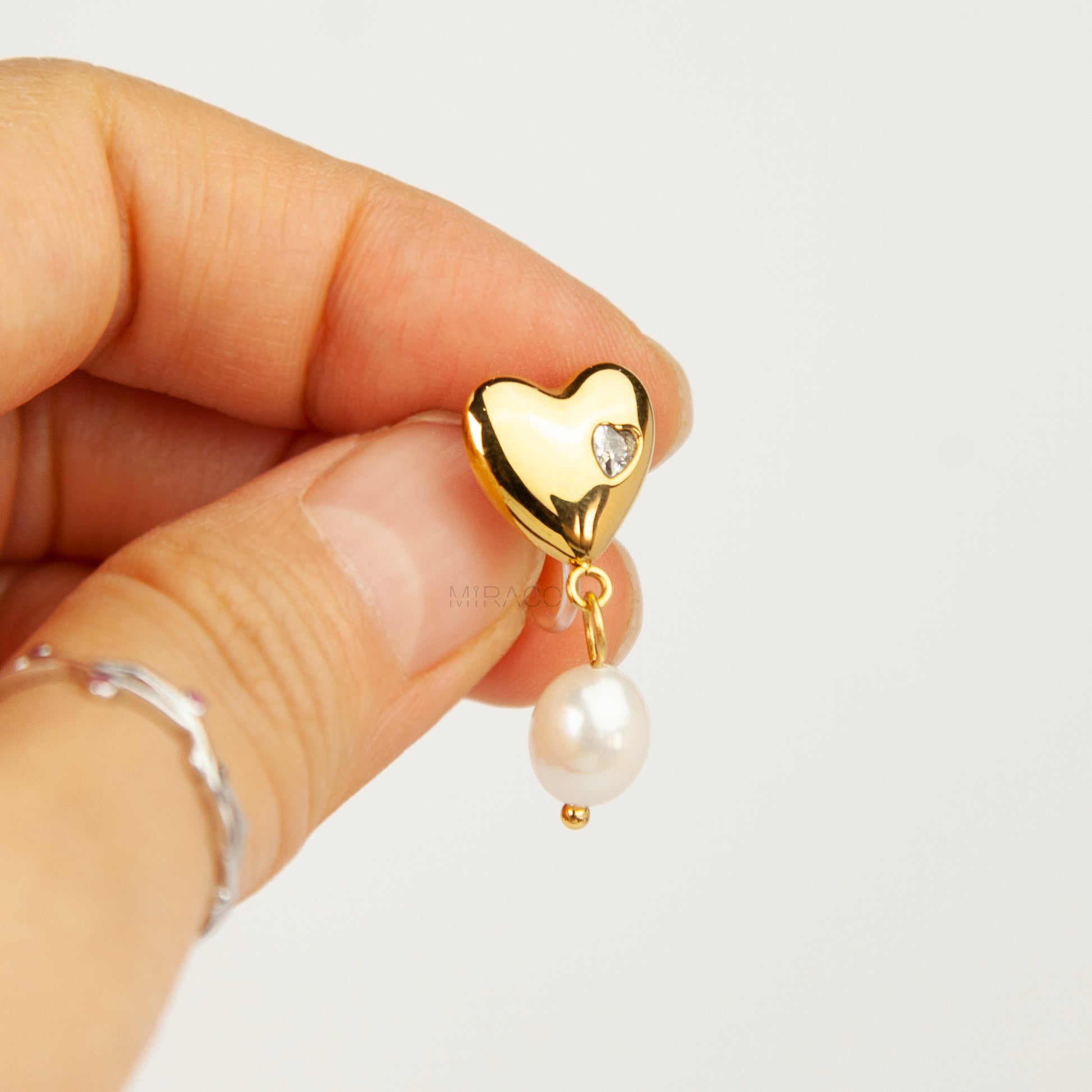 Pair of polished gold puffy heart clip-on earrings with star-set cz detail and dangling white pearls featuring clear invisible resin backs for non-pierced ears against a white backdrop.