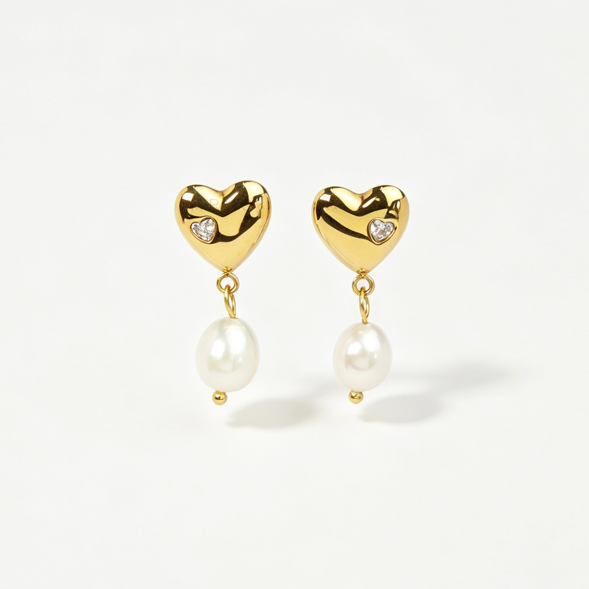 Pair of polished gold puffy heart clip-on earrings with star-set cz detail and dangling white pearls featuring clear invisible resin backs for non-pierced ears against a white backdrop.
