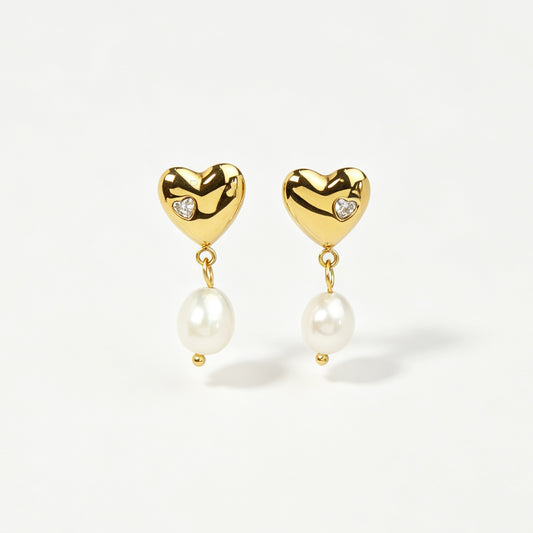 Pair of polished gold puffy heart clip-on earrings with star-set cz detail and dangling white pearls featuring clear invisible resin backs for non-pierced ears against a white backdrop.