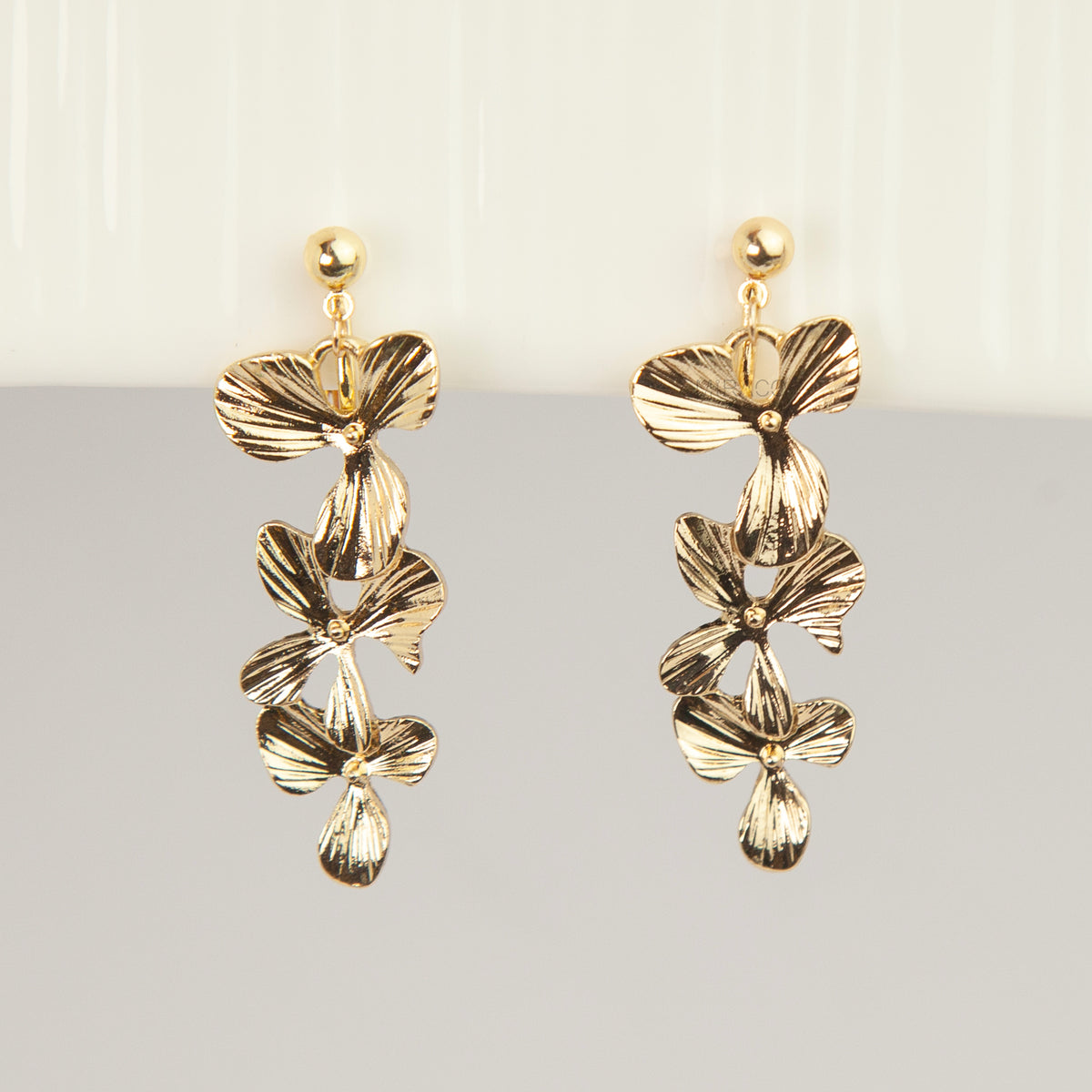 Pair of gold textured floral clip-on earrings with adjustable screw-back closures showing cascading layered flower petals on a clean neutral background