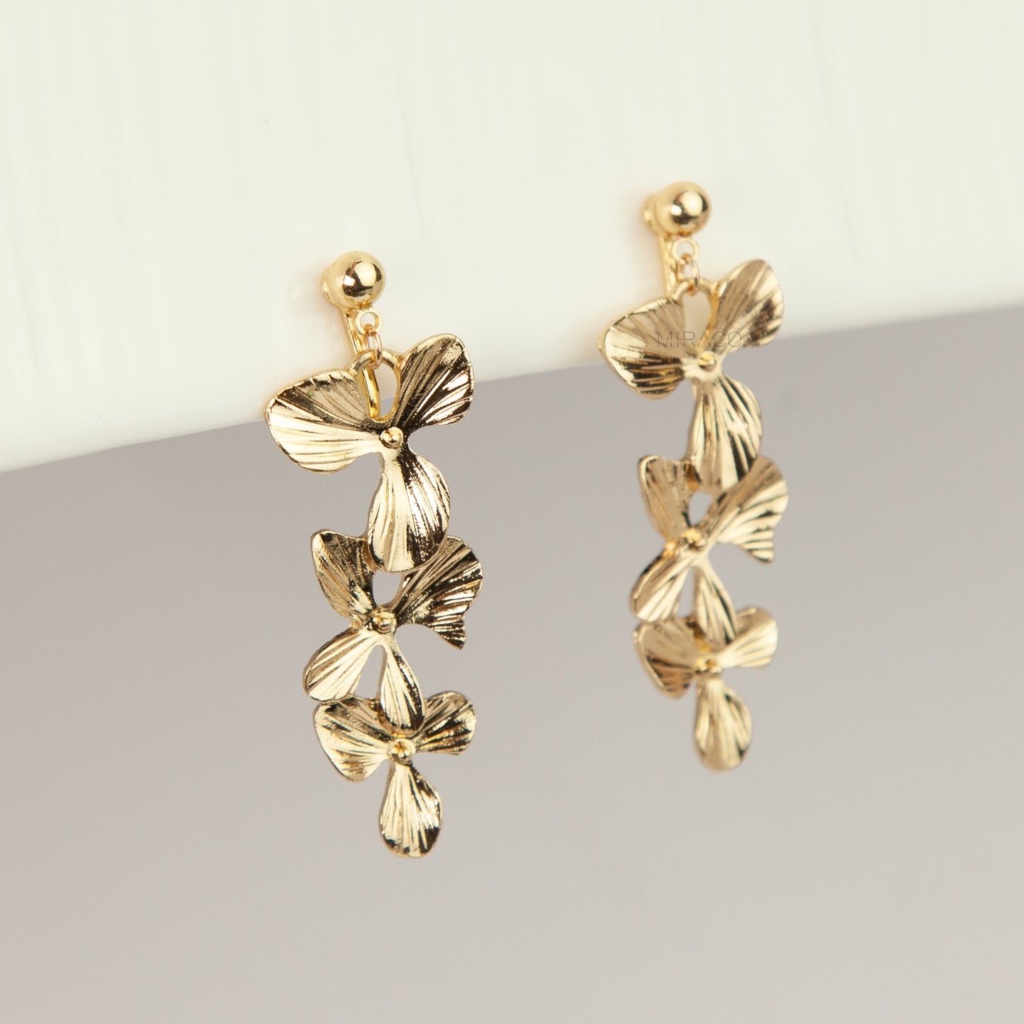 Pair of gold textured floral clip-on earrings with adjustable screw-back closures showing cascading layered flower petals on a clean neutral background