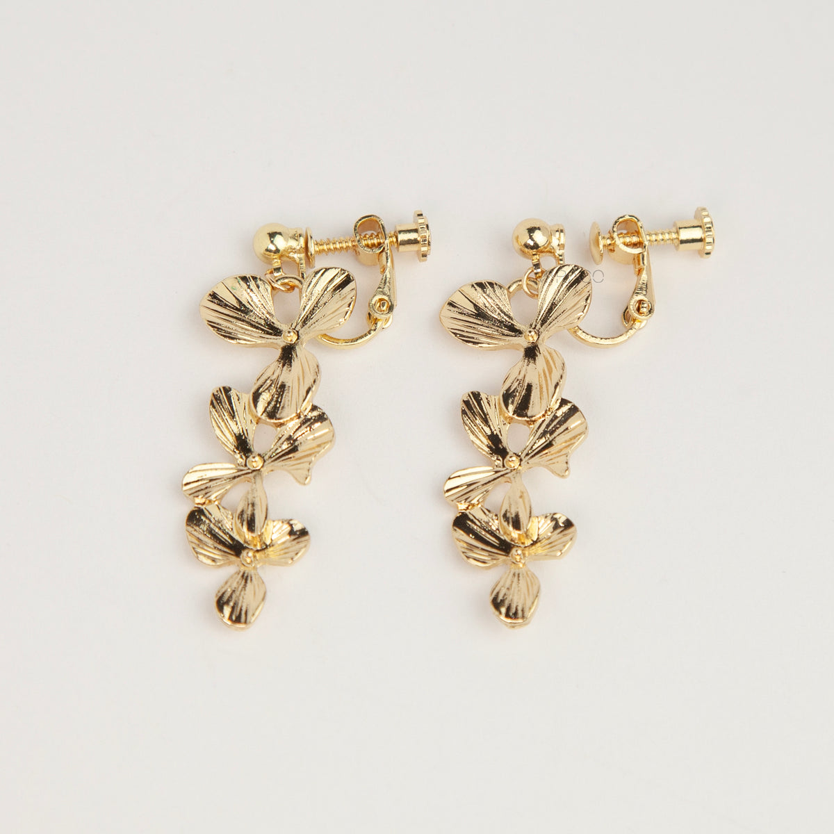 Pair of gold textured floral clip-on earrings with adjustable screw-back closures showing cascading layered flower petals on a clean neutral background