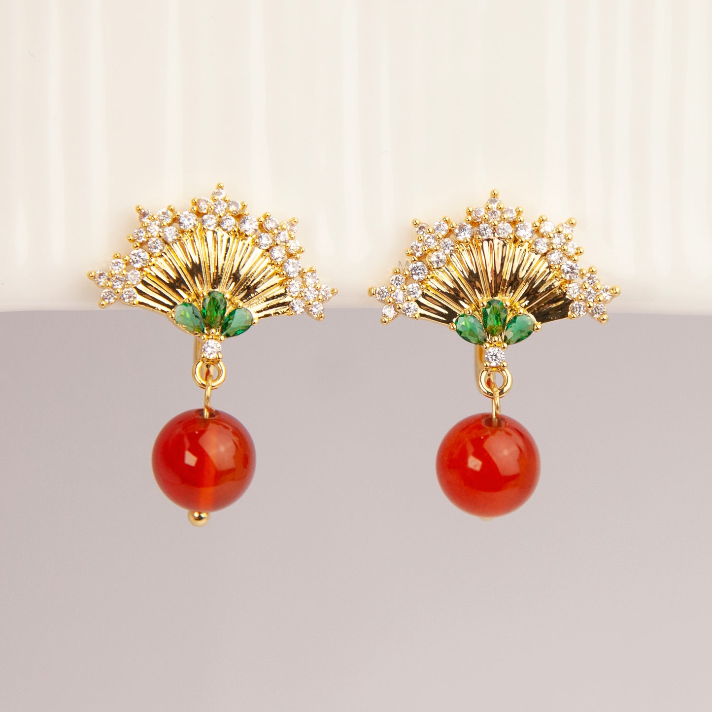 Gold Art Deco fan-shaped clip-on earrings with green crystal accents, pavé CZ trim, and hanging red agate bead drops 