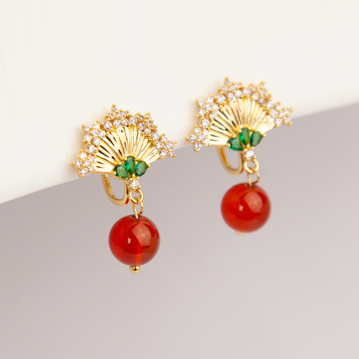 Gold Art Deco fan-shaped clip-on earrings with green crystal accents, pavé CZ trim, and hanging red agate bead drops 
