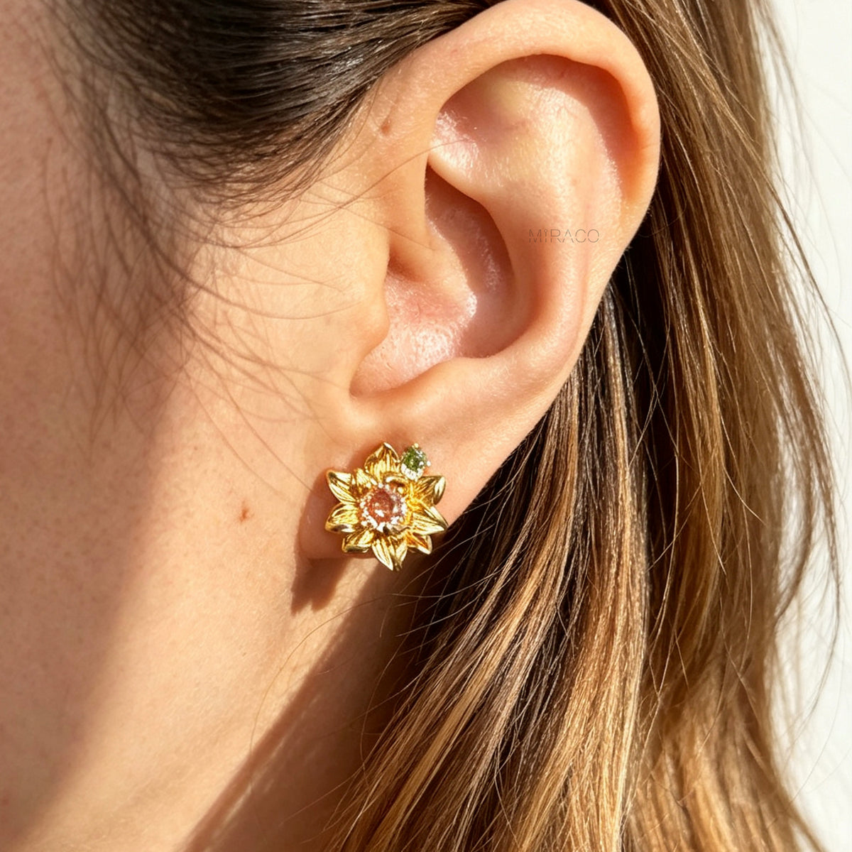 Pair of detailed gold sunflower clip-on stud earrings with amber crystal centers and olive green stone accents worn on an ear model