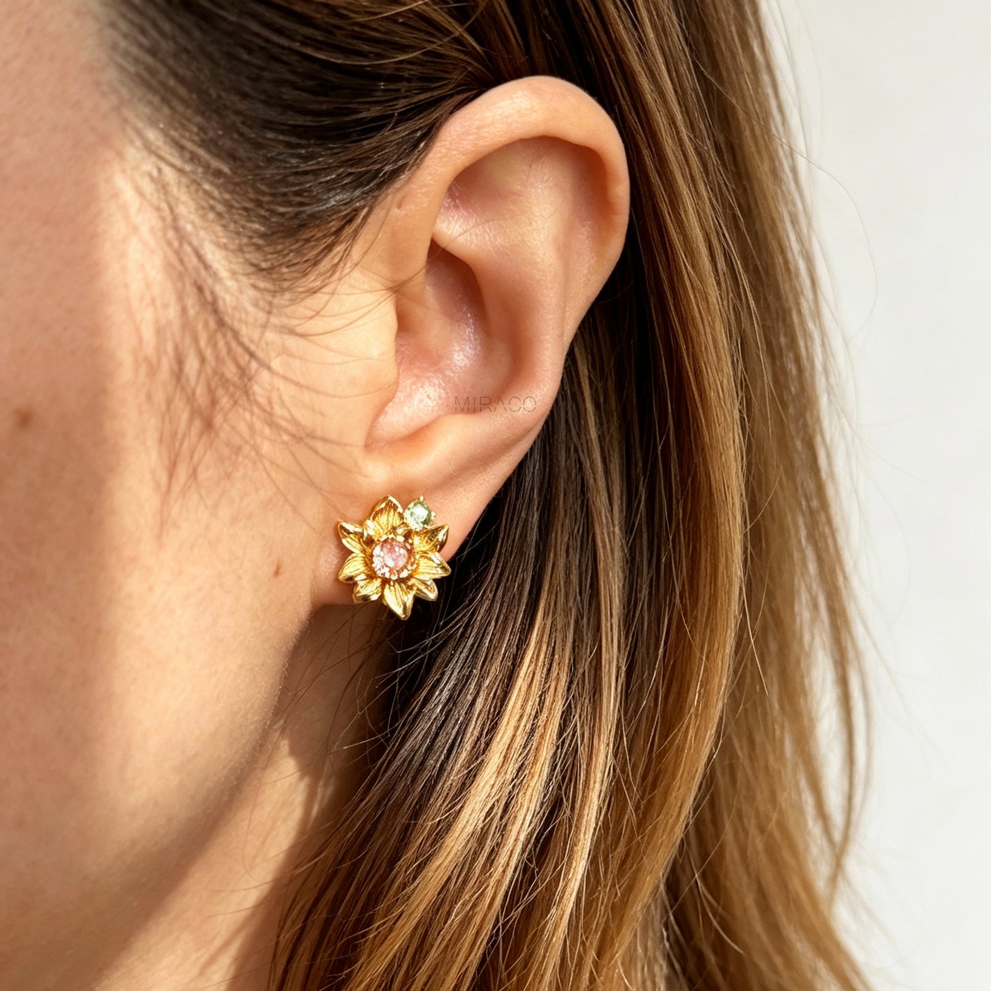 Pair of detailed gold sunflower clip-on stud earrings with amber crystal centers and olive green stone accents worn on an ear model