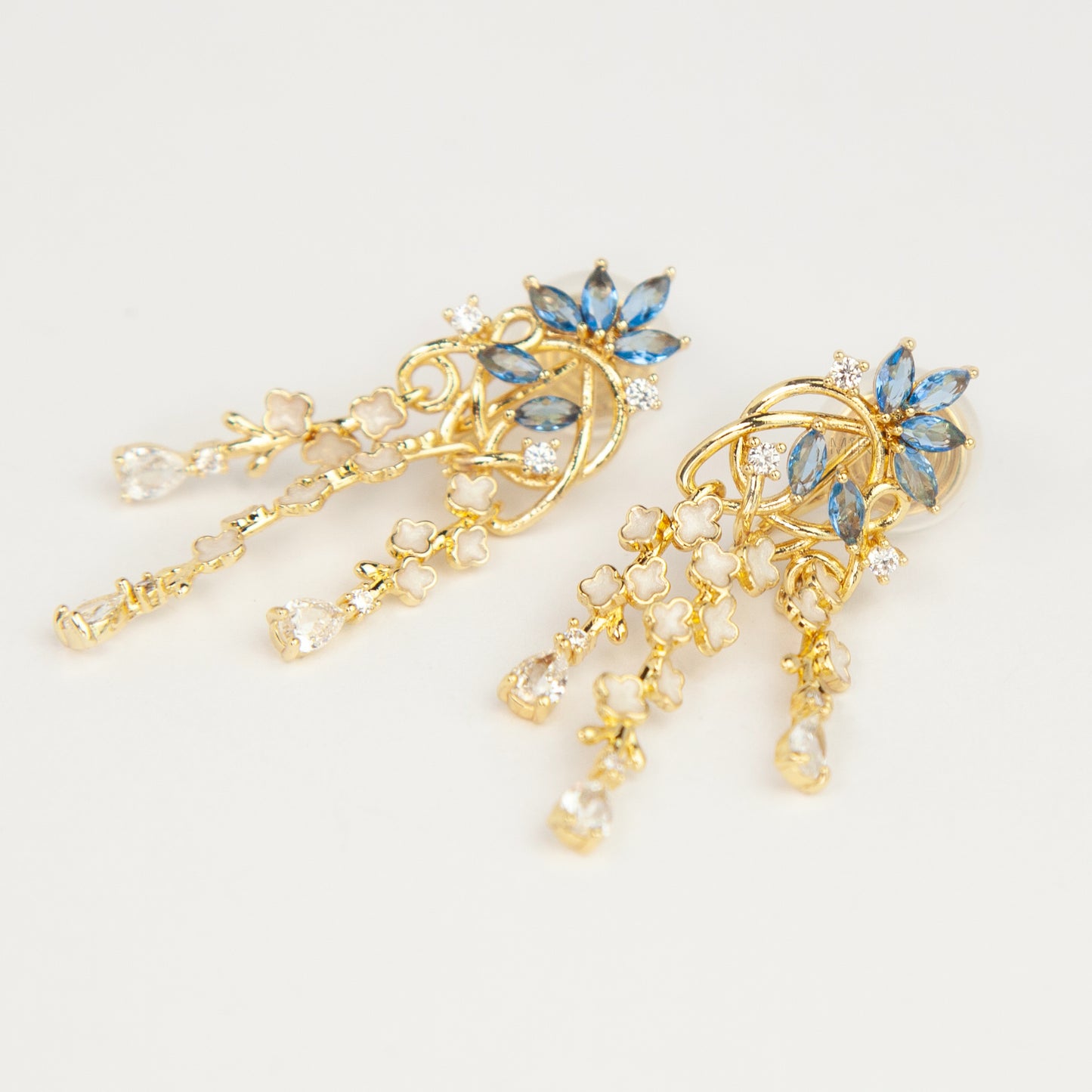 Gold coil-back clip-on chandelier earrings featuring blue marquise petals and cascading white flower dangles with teardrop crystals 