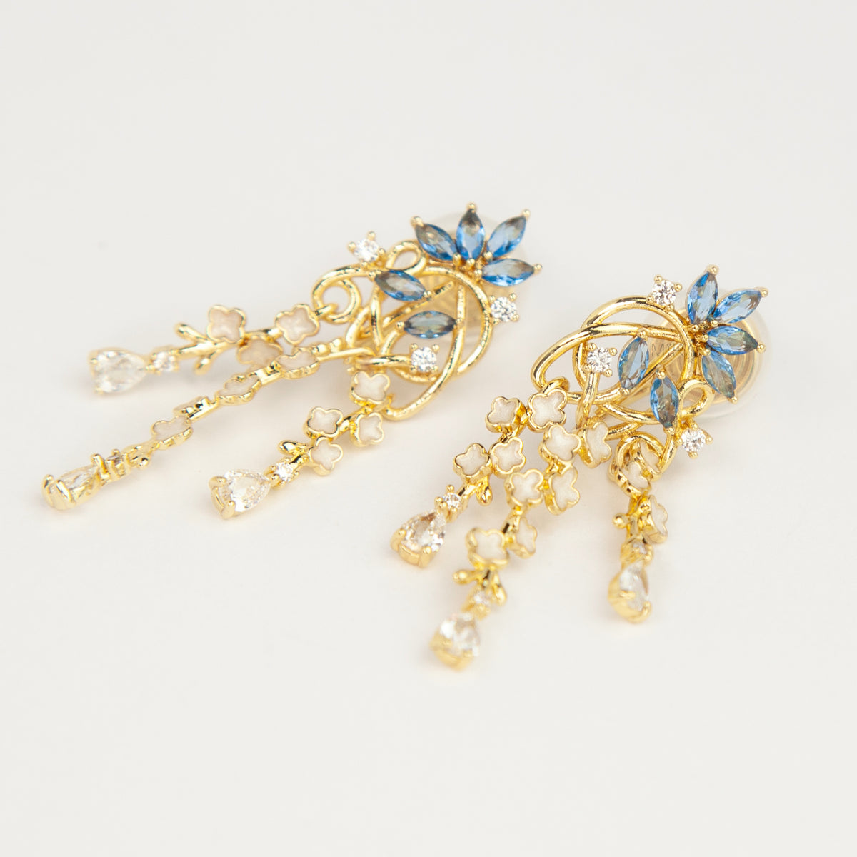 Gold coil-back clip-on chandelier earrings featuring blue marquise petals and cascading white flower dangles with teardrop crystals 