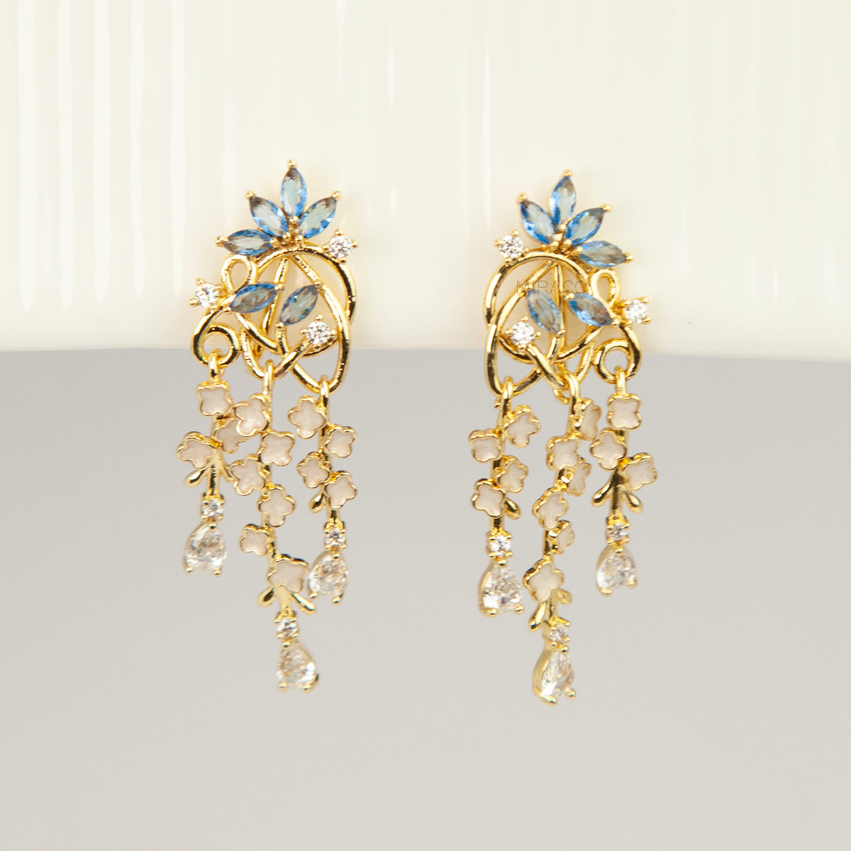 Gold coil-back clip-on chandelier earrings featuring blue marquise petals and cascading white flower dangles with teardrop crystals 