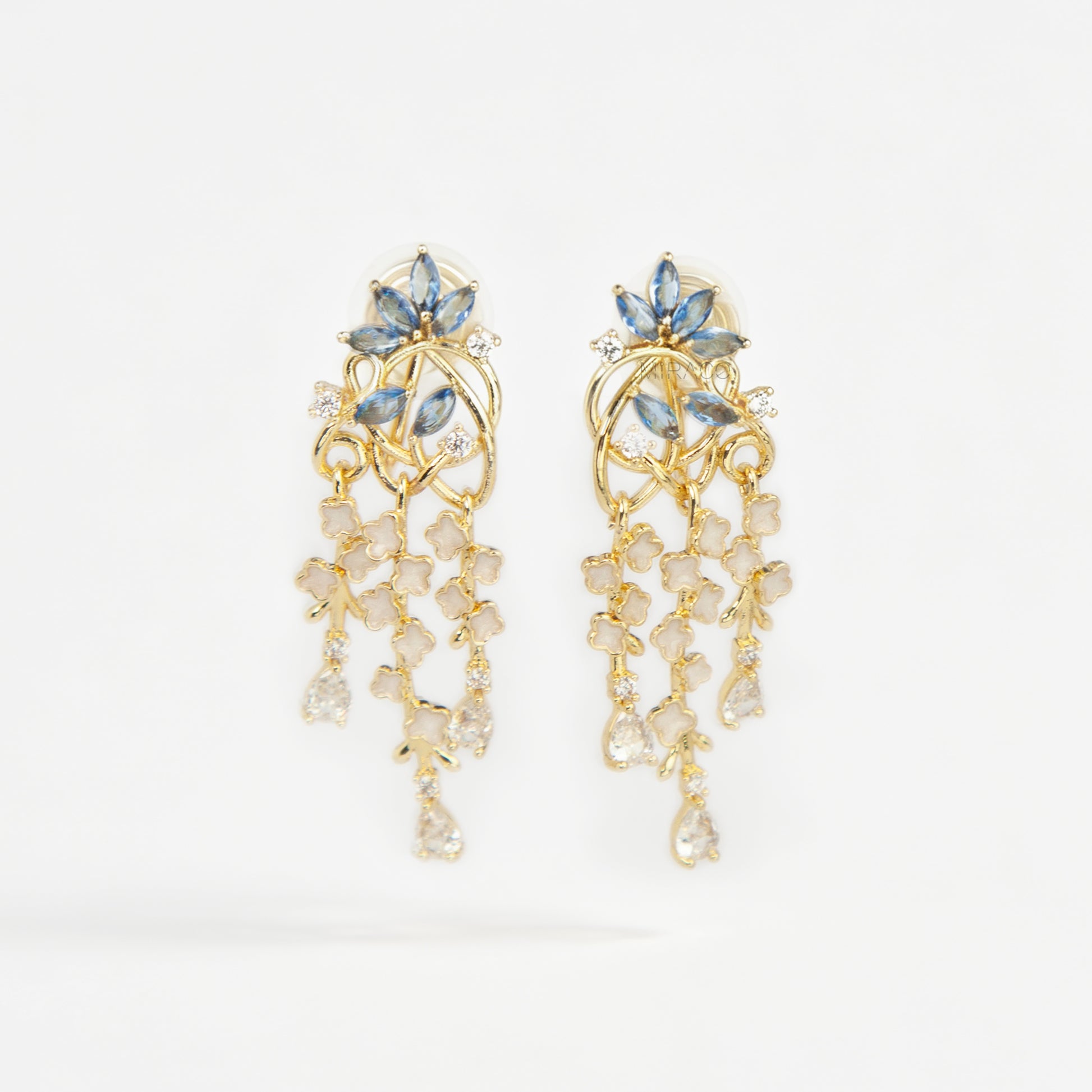 Gold coil-back clip-on chandelier earrings featuring blue marquise petals and cascading white flower dangles with teardrop crystals