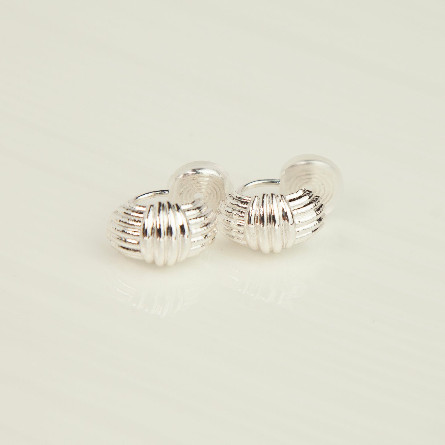 A pair of silver hoop earrings with a textured, ribbed design, displayed on a clean, light off-white surface.