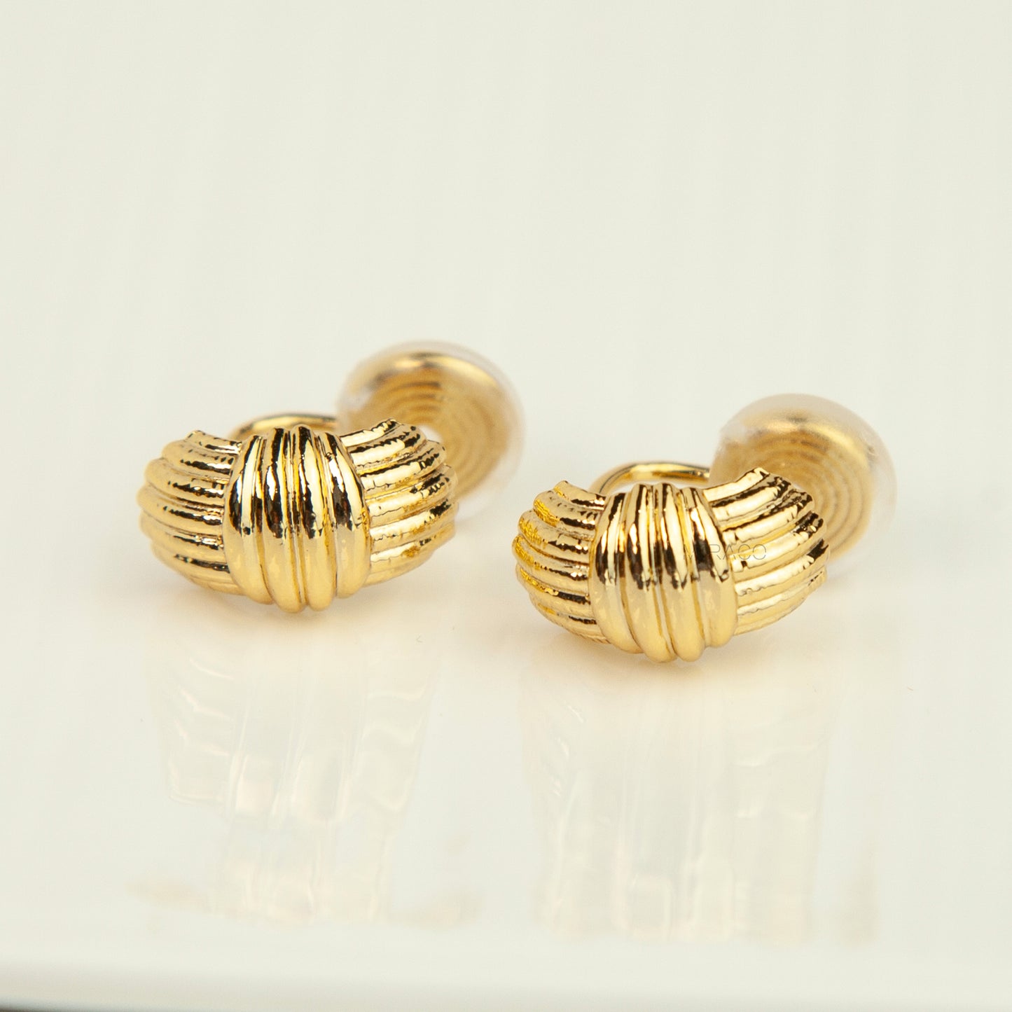 A pair of gold cufflinks with a textured, ribbed oval design, displayed on a clean white reflective surface.
