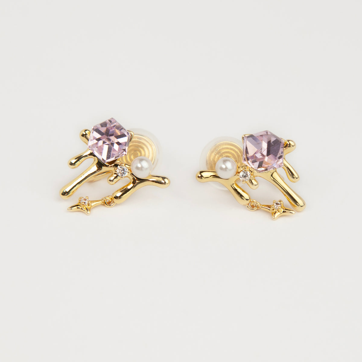 Gold coil-back clip-on earrings featuring a molten liquid drip design with a geometric pink crystal, white pearl, and dangling starburst charm.