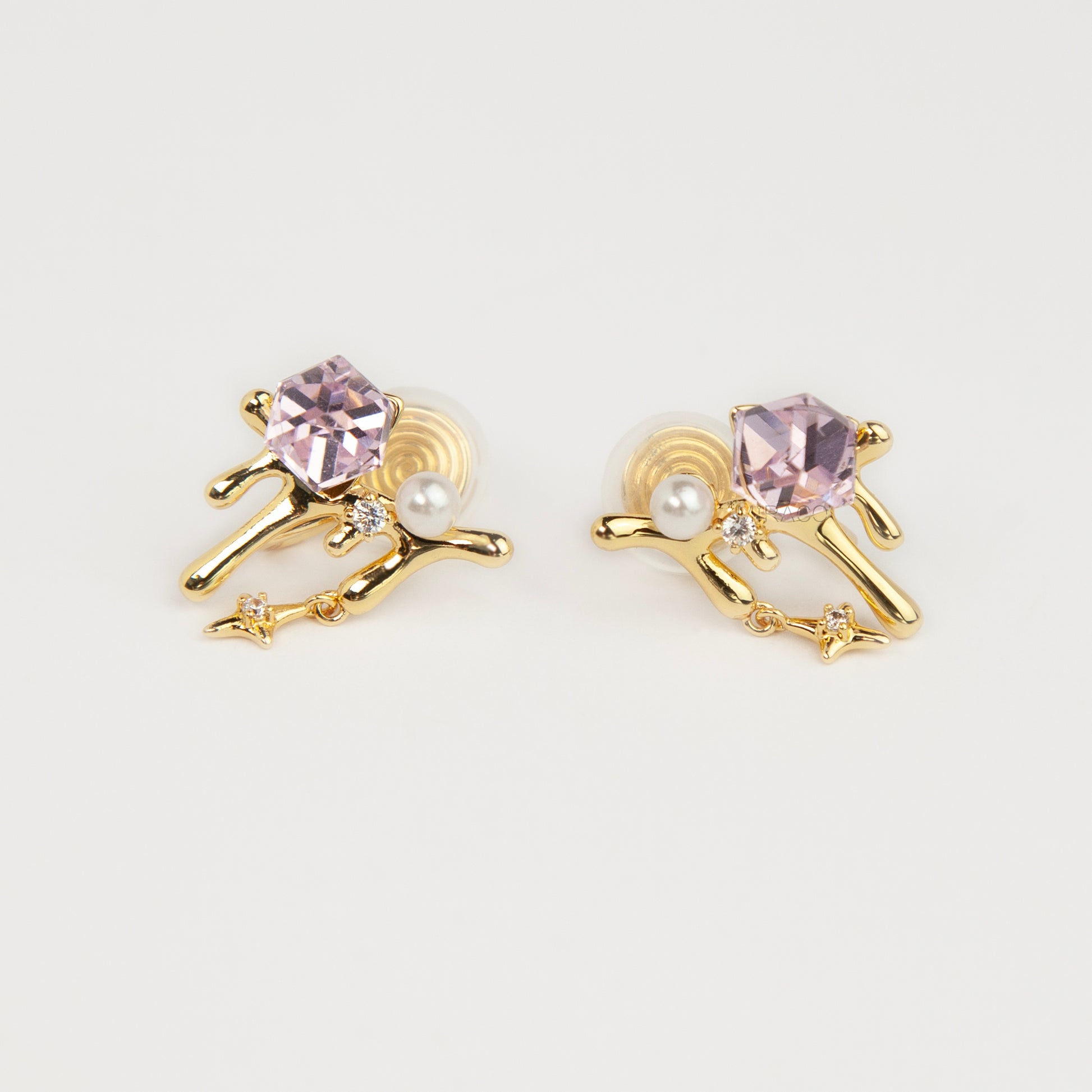 Gold coil-back clip-on earrings featuring a molten liquid drip design with a geometric pink crystal, white pearl, and dangling starburst charm.