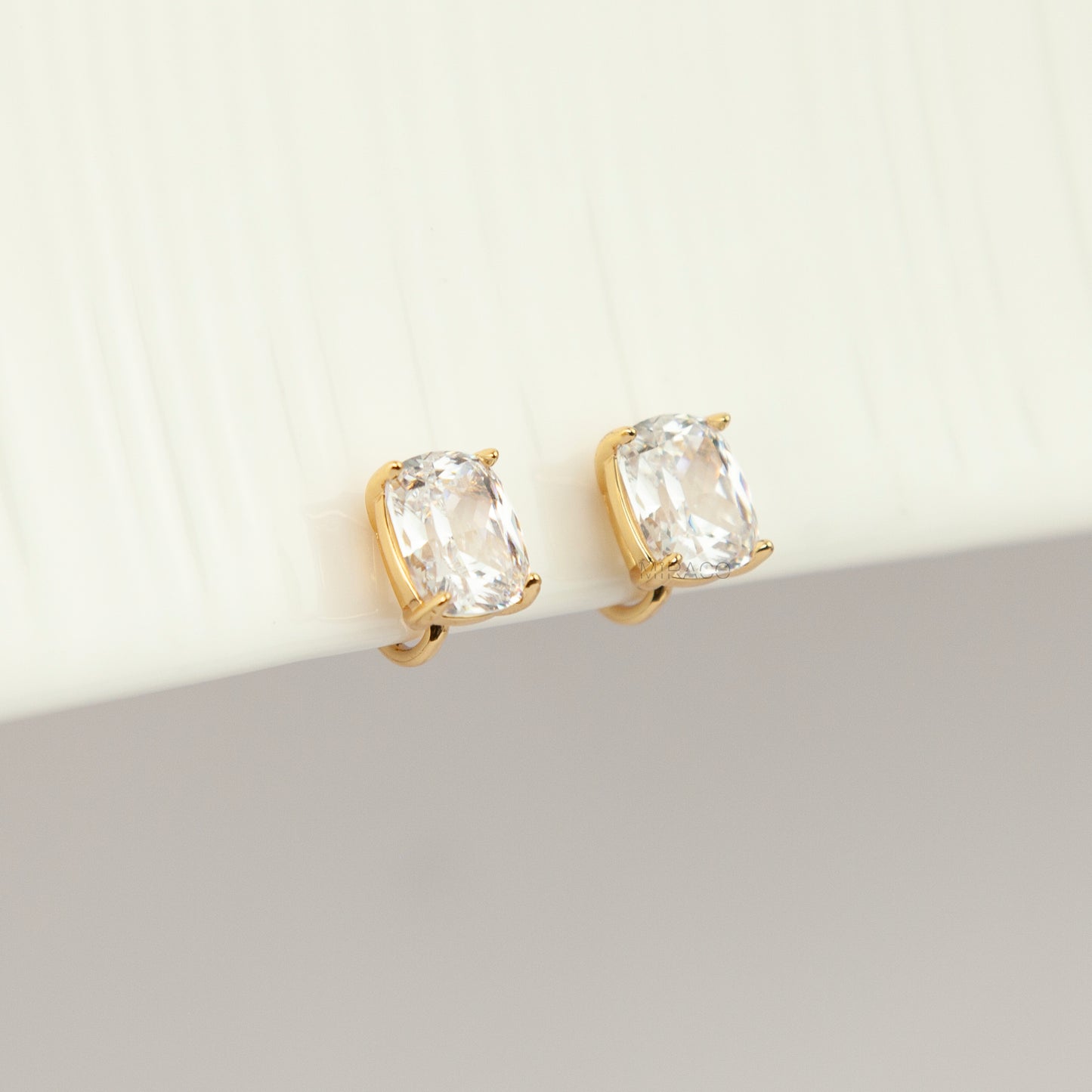 Gold-tone clip-on stud earrings set with large cushion-cut clear crystals and round silicone backs 