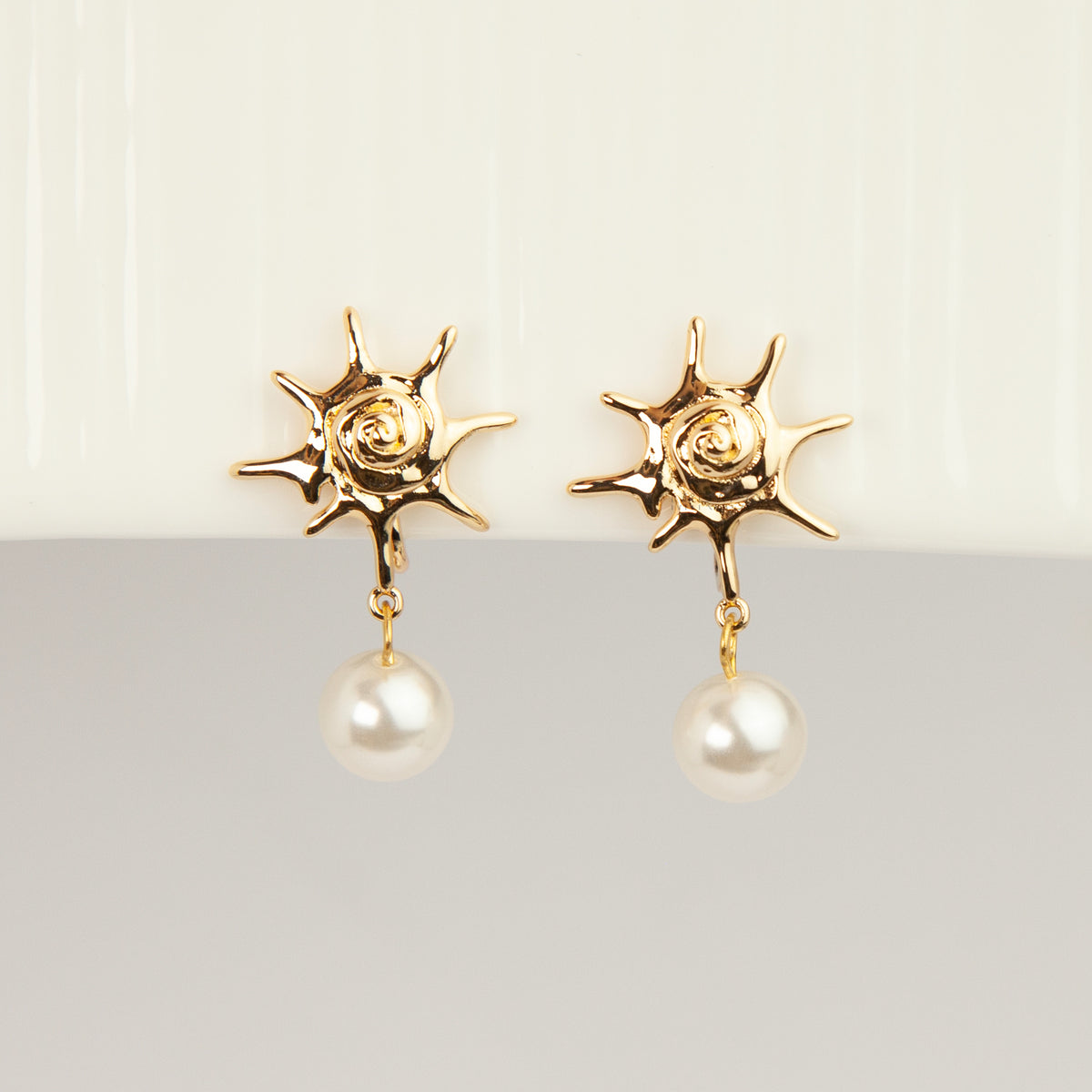 Gold coil-back clip-on earrings with a swirled sunburst star motif and a dangling white pearl