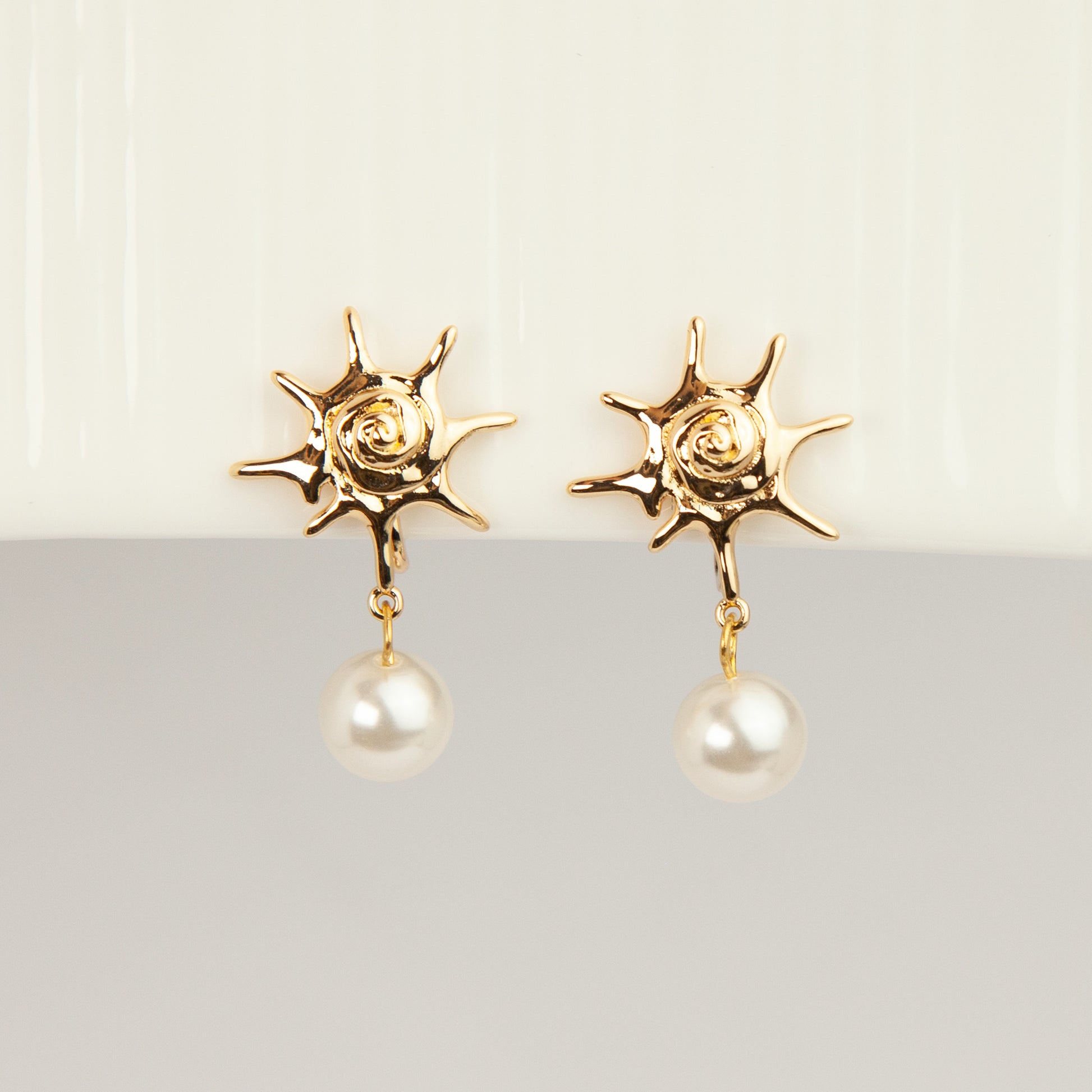 Gold coil-back clip-on earrings with a swirled sunburst star motif and a dangling white pearl