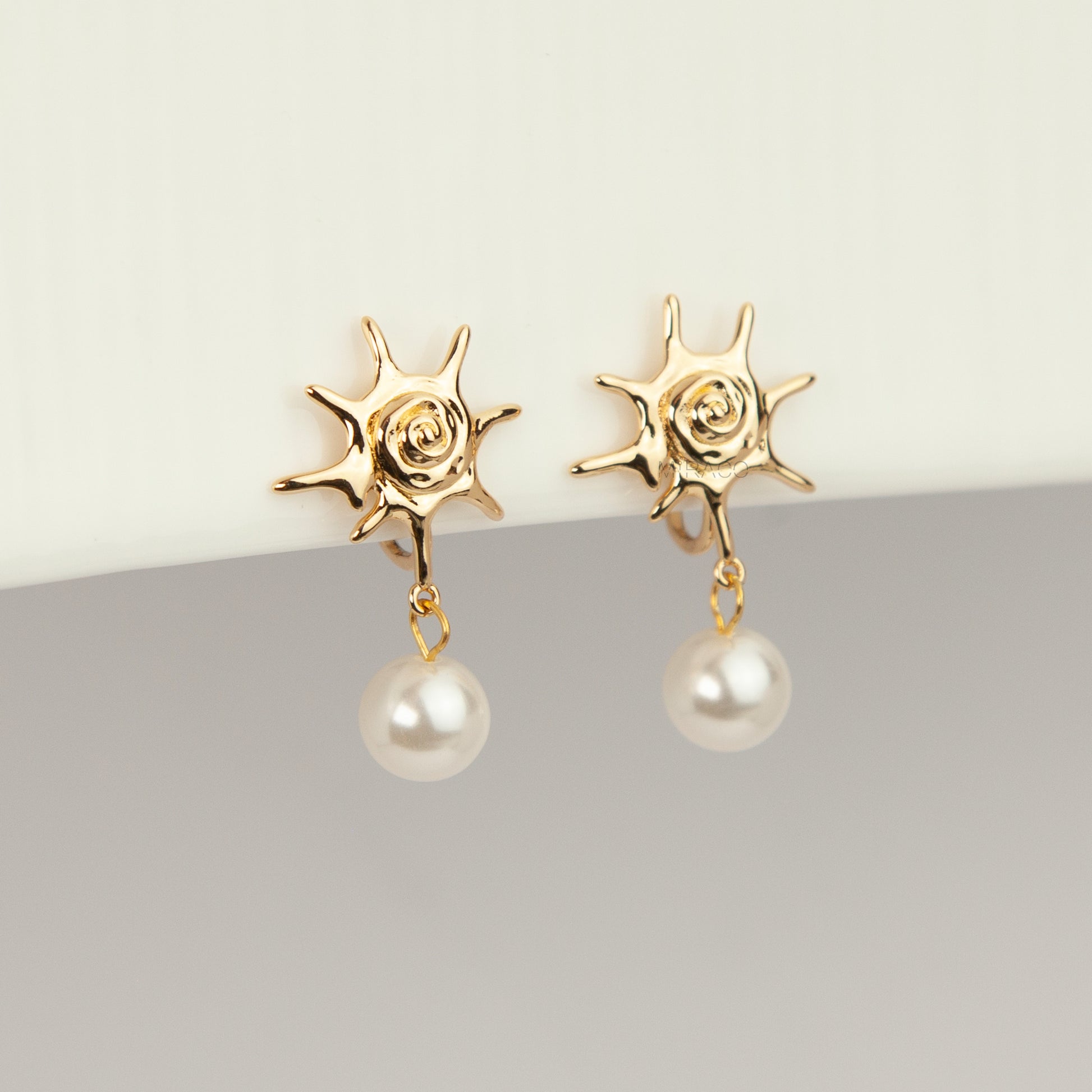 Gold coil-back clip-on earrings with a swirled sunburst star motif and a dangling white pearl